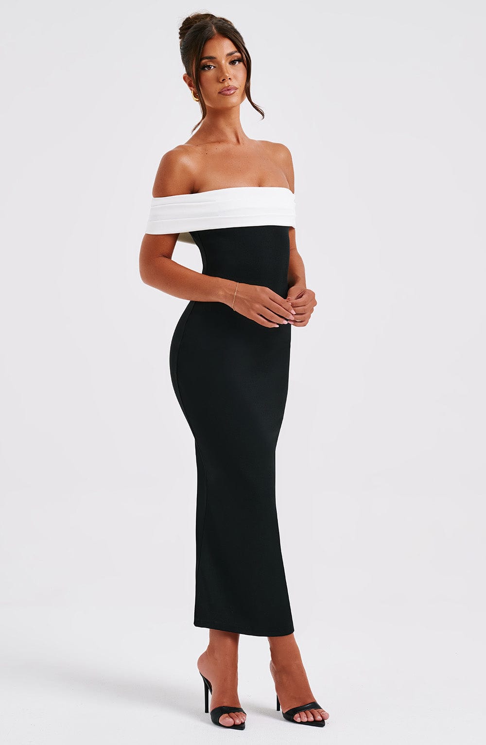 Side profile of a black off-the-shoulder midi dress with a white band, showcasing the elegant fit and subtle mermaid hem.