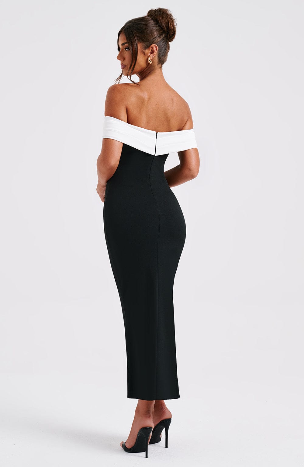 Three-quarter back view of a black off-the-shoulder midi dress, highlighting the fitted waist and a slight flare at the bottom.