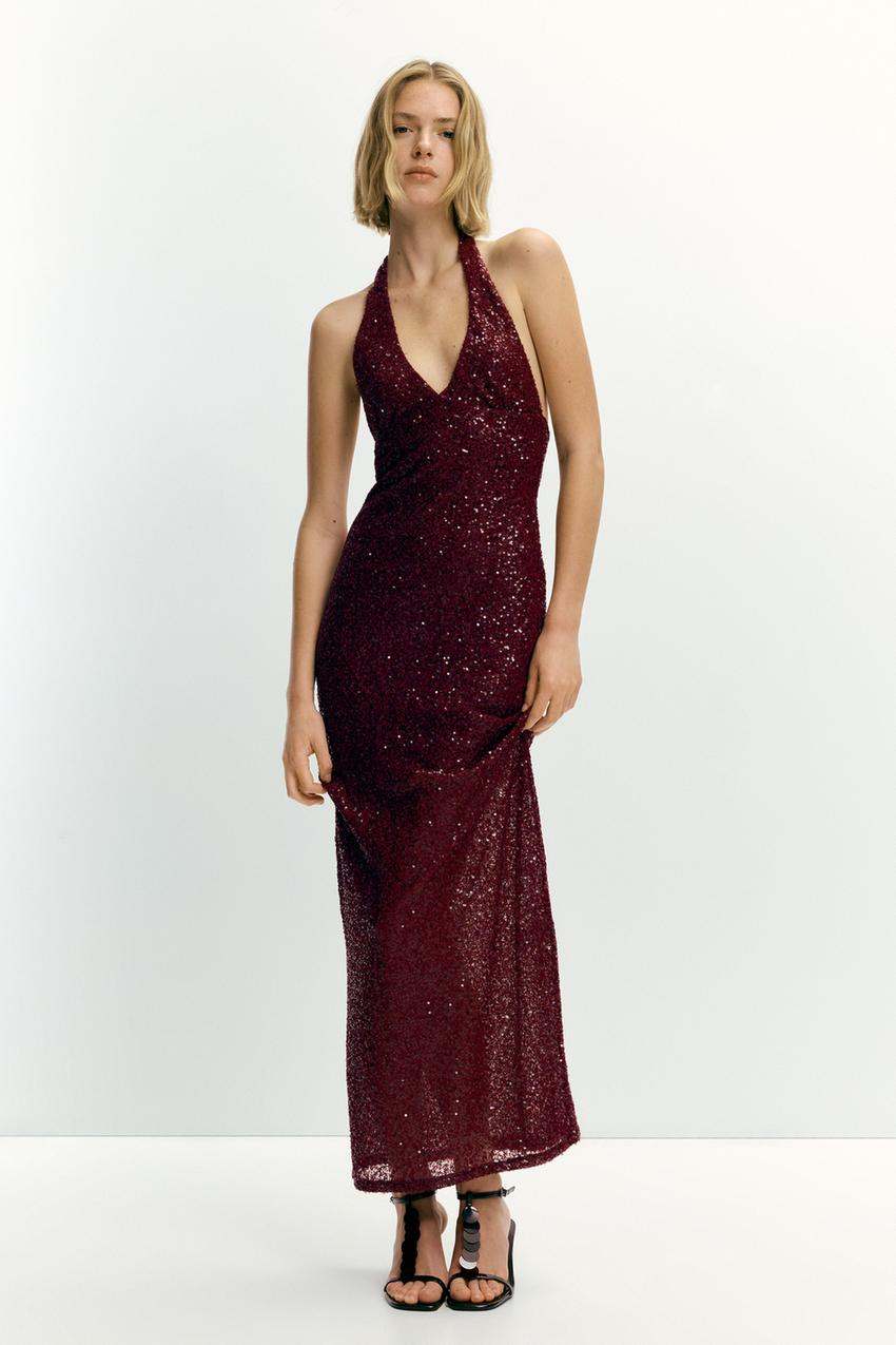 Burgundy sequin halter maxi dress with V-neckline on a woman posing frontally