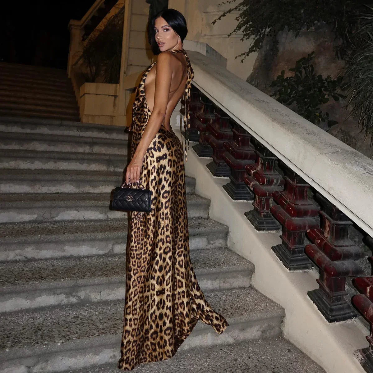 Back view of Jillian leopard print maxi dress, showing open back and tie details, with a long flowing skirt on stairs.