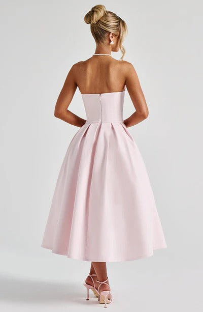 Back view of the light pink strapless midi dress, displaying the full pleated skirt and delicate heels.