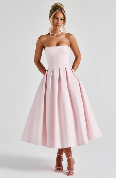 Full-length view of a light pink strapless midi dress with a pleated skirt and pearl necklace.