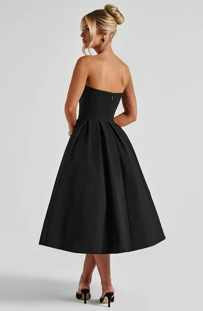 Rear view of a black strapless midi dress, showcasing the pleated skirt and back zipper detail.
