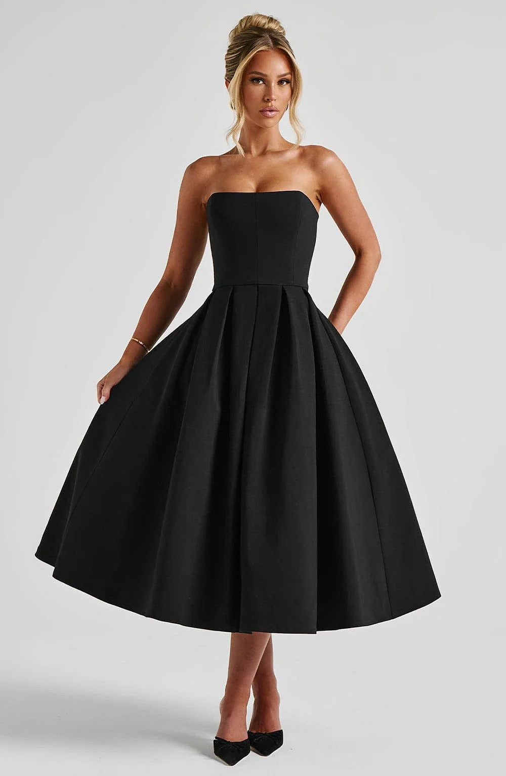 Front view of a black strapless midi dress with a pleated A-line skirt and sweetheart neckline.