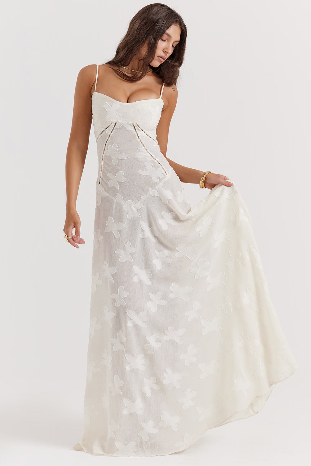 Angled view of the ivory Juliet Lace Maxi Dress, with a hand holding the skirt to emphasize the butterfly lace.