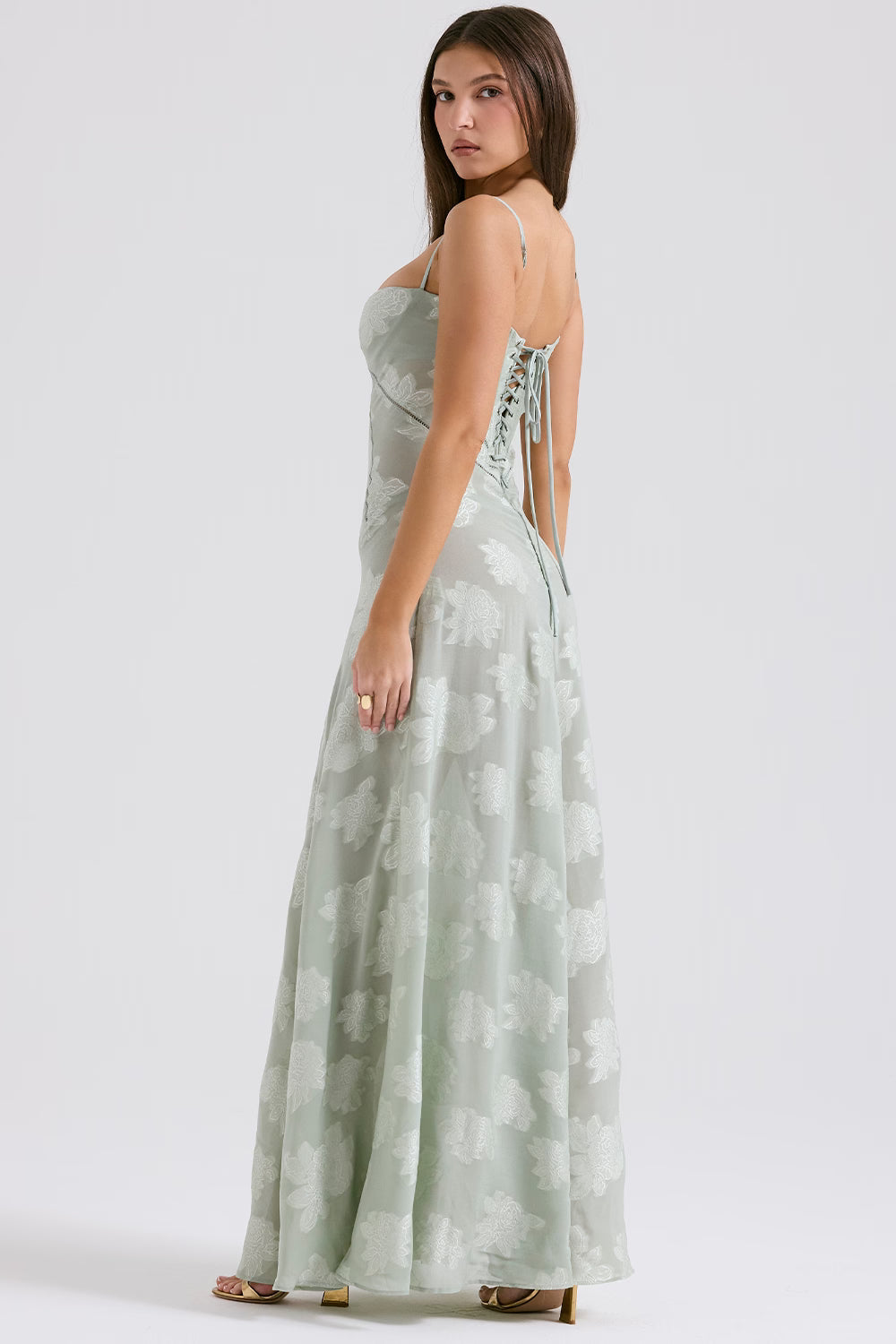 Side view of a light sage green Juliet Lace Maxi Dress, featuring a delicate floral pattern and a lace-up back closure.