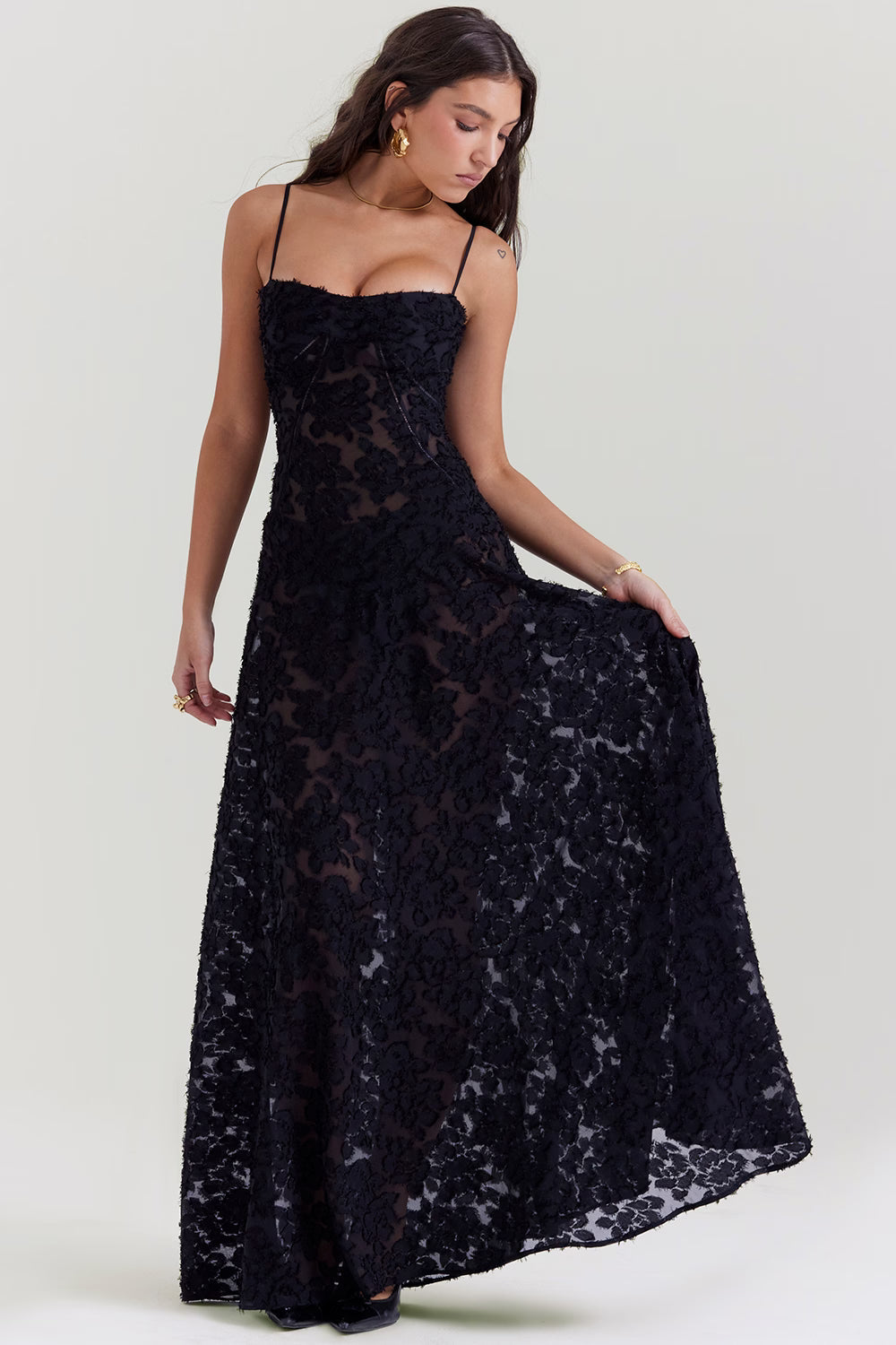 Front view of the black Juliet Lace Maxi Dress, with a hand gently lifting the skirt to show the sheer lace detail.