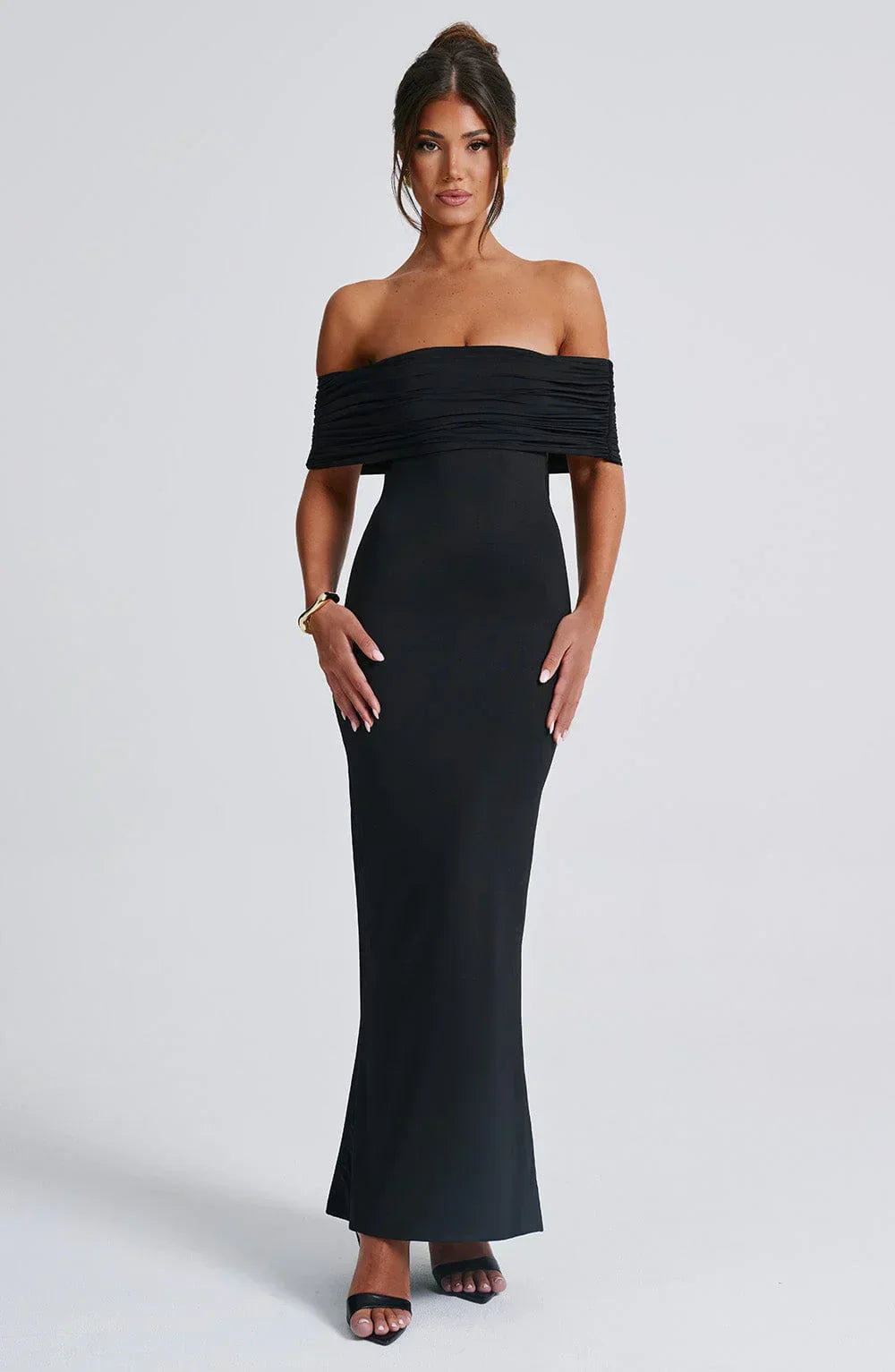 Front view of a women's sophisticated black Karina maxi dress with a pleated off-the-shoulder design and a sleek, form-fitting cut, with gold bracelet.