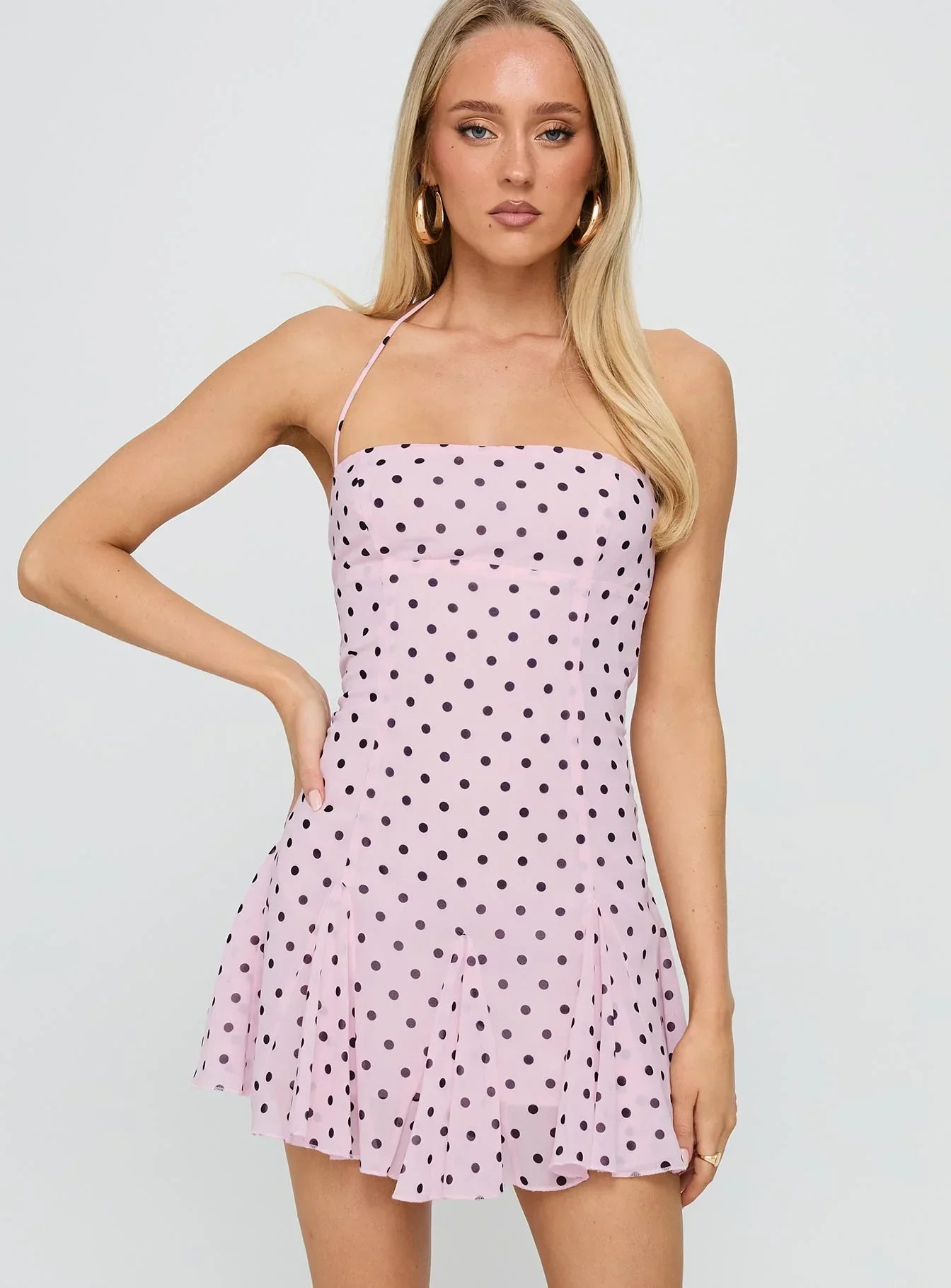 Front view of a light pink polka dot mini dress with black spots, featuring a square neckline and halter straps.