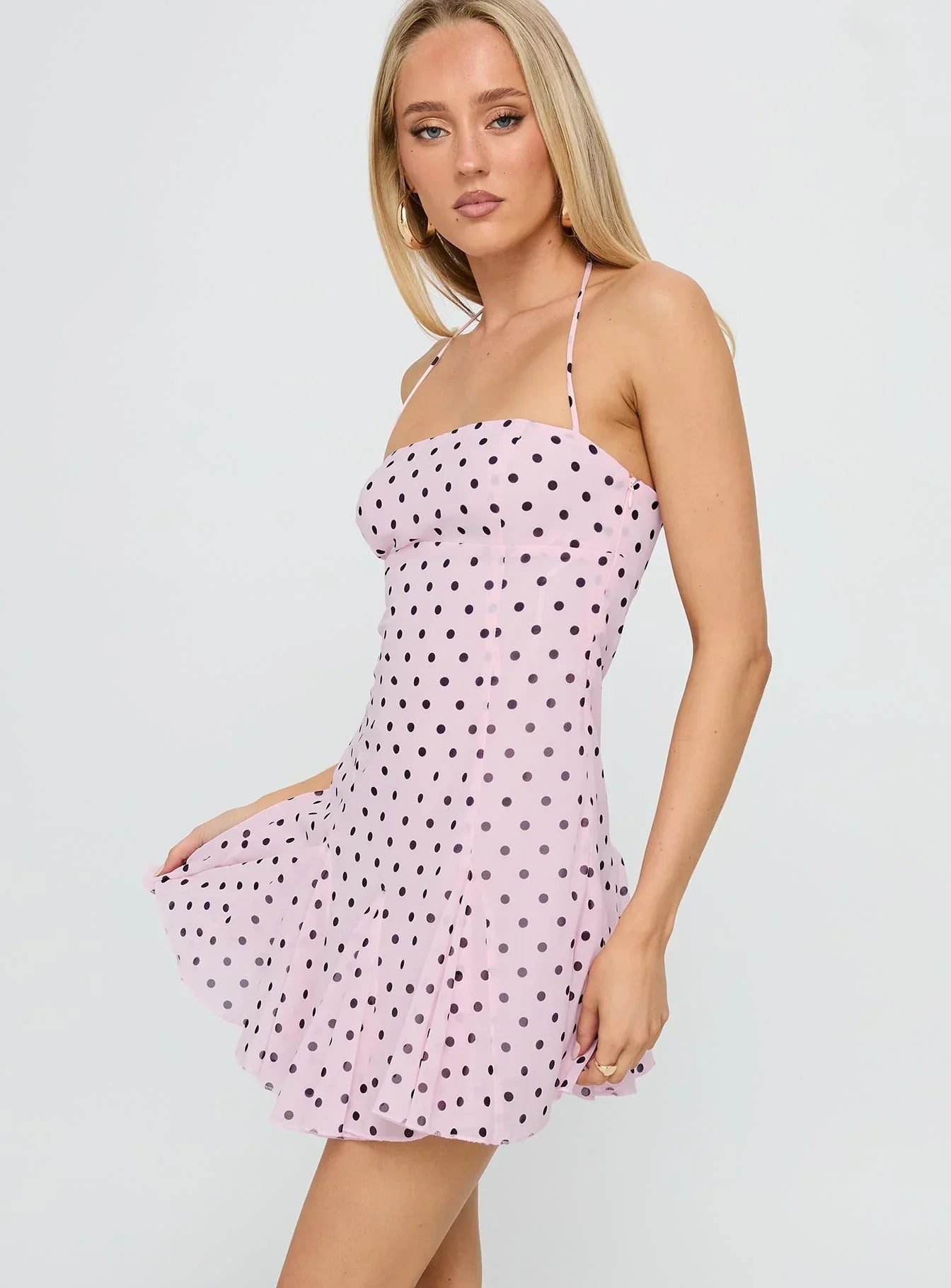 Front view of a light pink polka dot mini dress with black spots, featuring a square neckline and halter straps, with skirt lifted slightly.