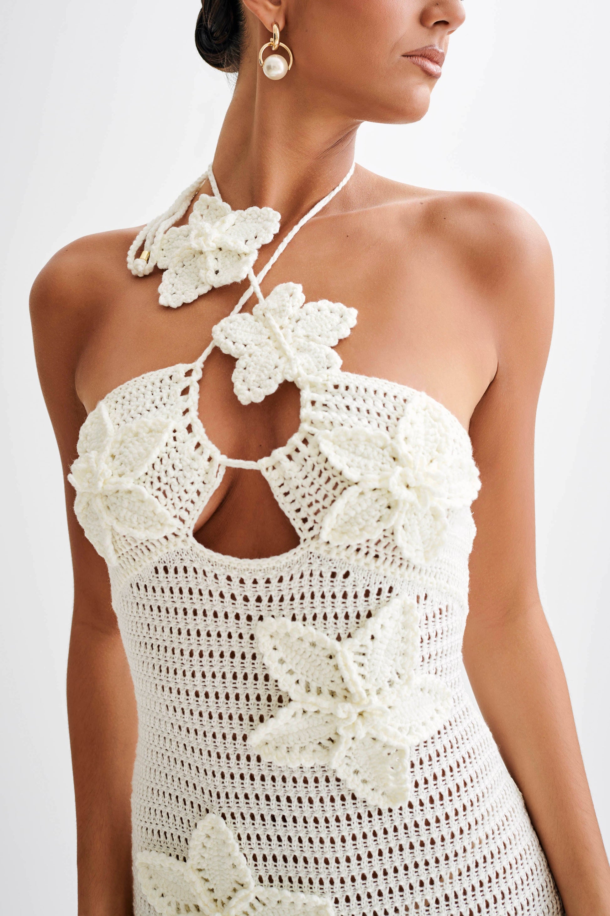 Close-up of a white crochet maxi dress, featuring a halter neckline with 3D floral appliques and a keyhole cutout.