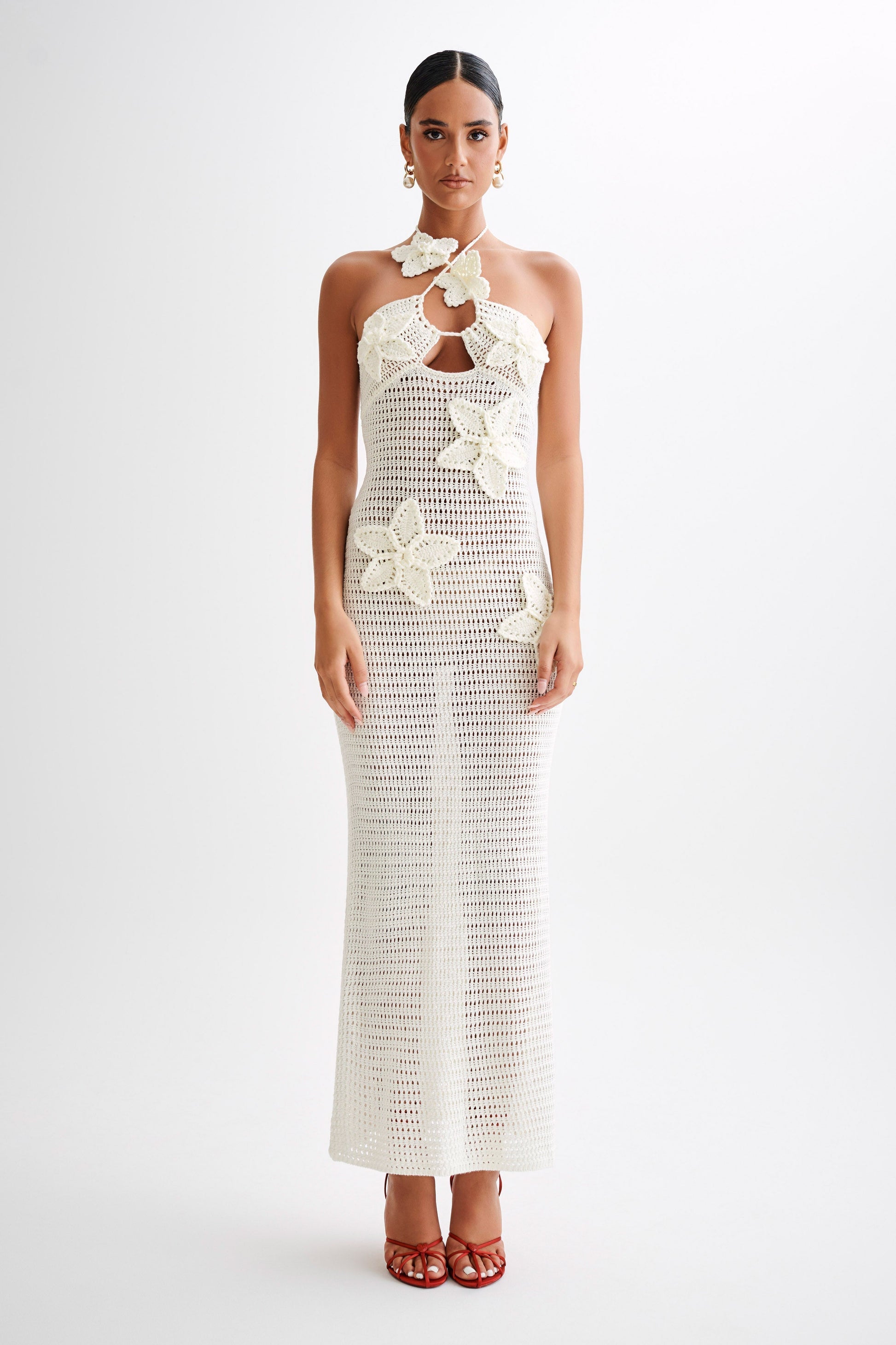 Front view of an ivory crochet maxi dress featuring large floral appliques and a halter neck, suitable for a resort or vacation.