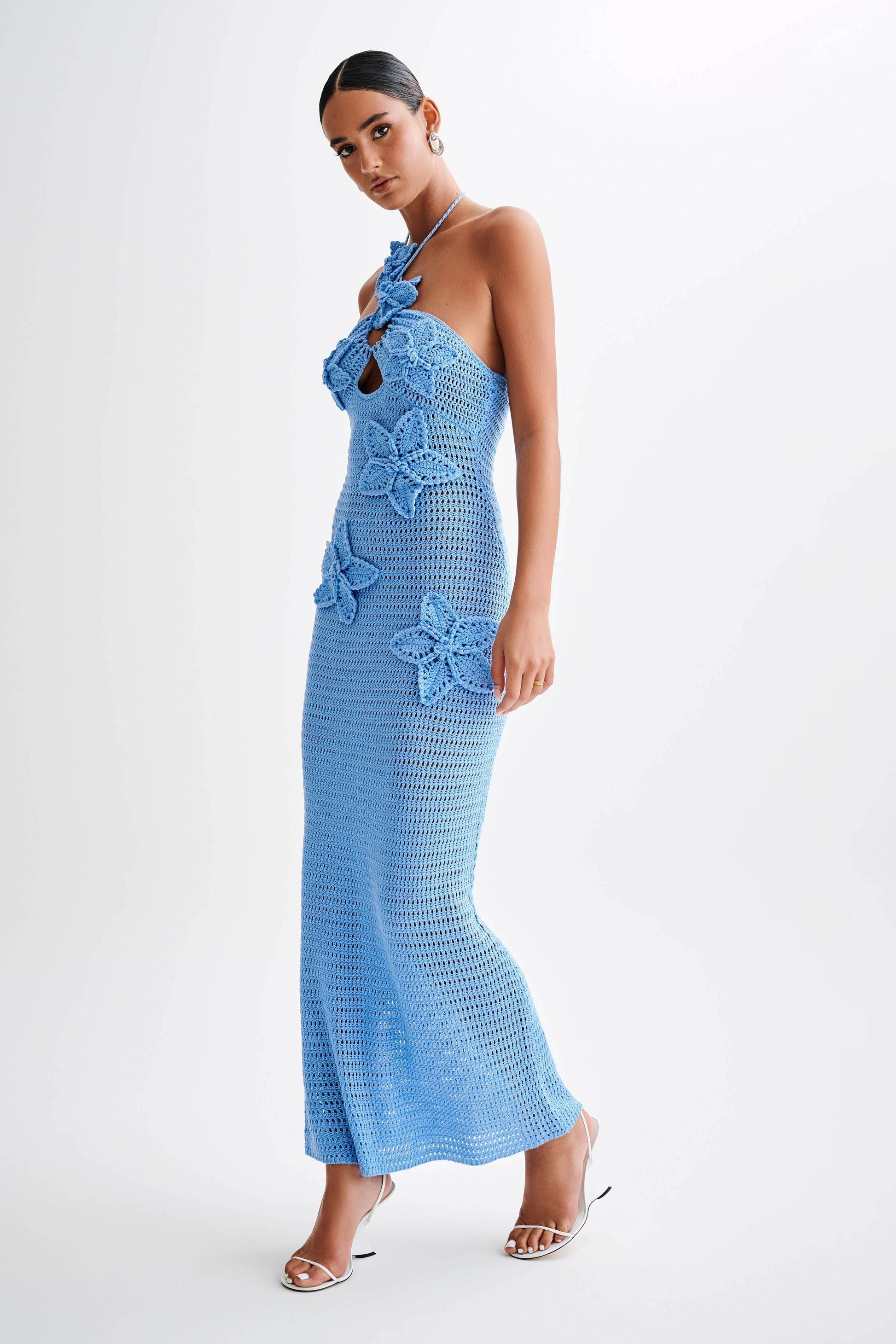 Side profile of a woman in a light blue crochet maxi dress with floral details and a halter neckline, a fashionable dress.