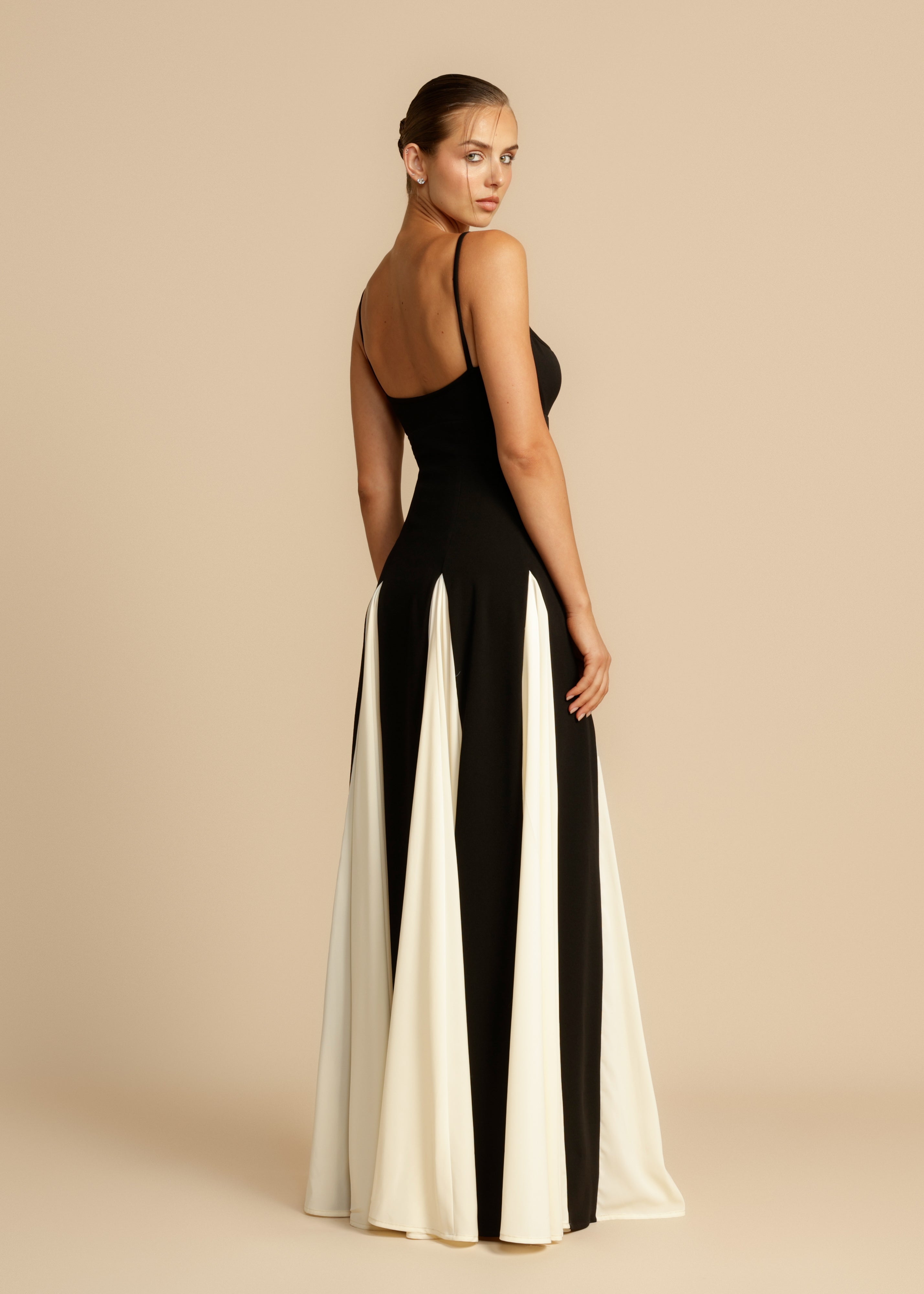 Back 3/4 view of a black and white paneled maxi dress featuring a low back and flowing skirt panels.