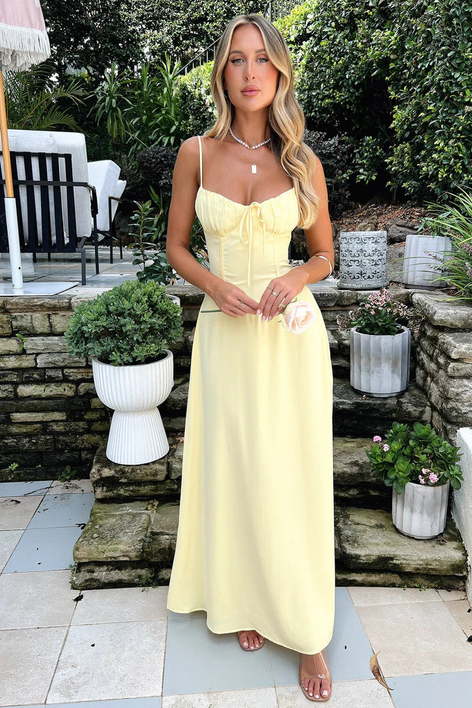 Front view of a pale yellow Kora Ruched Maxi Dress featuring a tie-front bust and corset-style waist details.