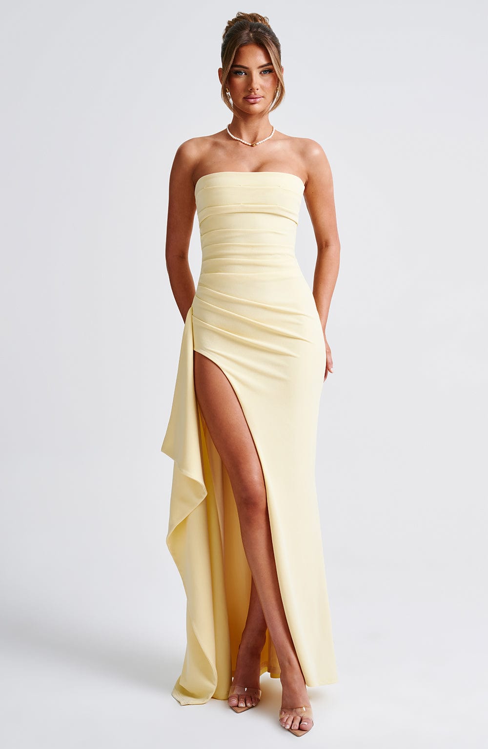 Pale yellow strapless maxi dress with draped side slit and ruched bodice detail, perfect for a formal event.