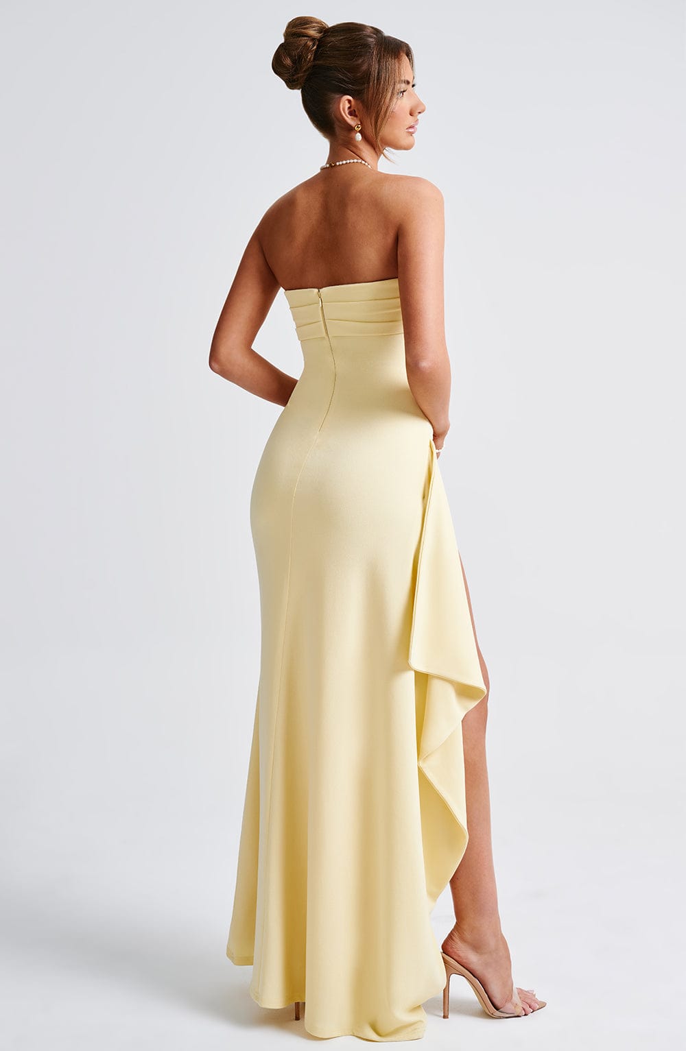 Back view of a pale yellow strapless maxi dress with a draped side detail and a subtle train, ideal for a wedding or formal event.