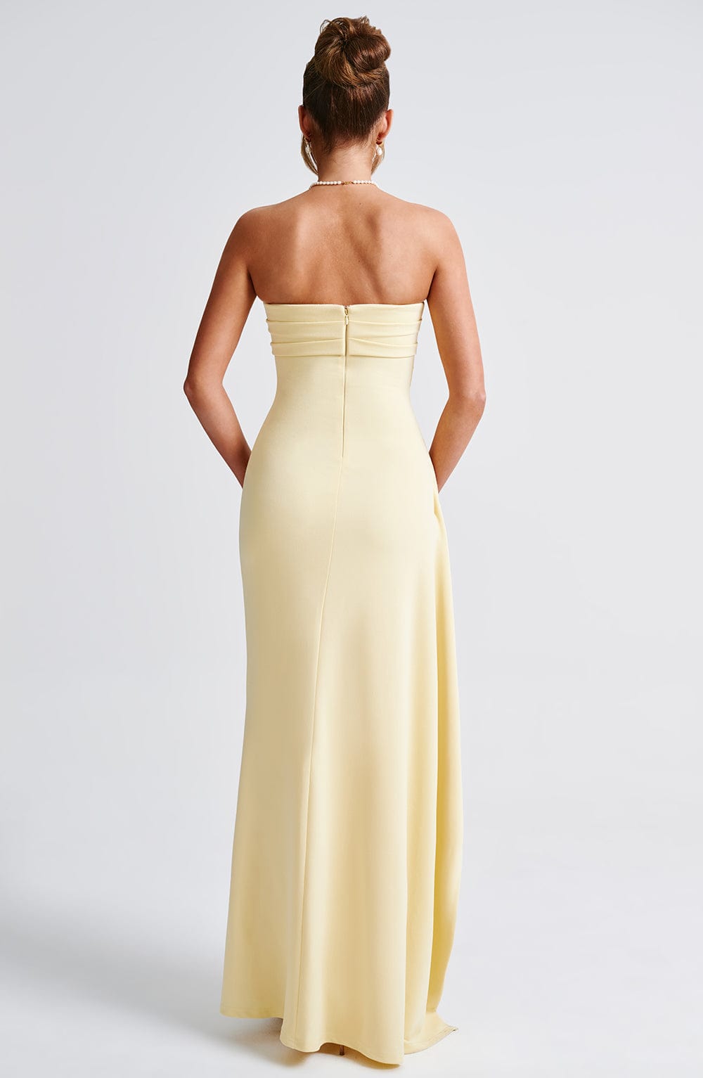 Rear view of a pale yellow strapless maxi dress, showing the smooth, fitted silhouette and floor-length design.