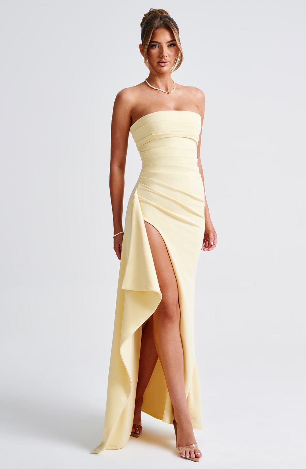 Front view of the Kyla Draped Maxi Dress, a light yellow strapless gown with elegant side draping and high leg slit