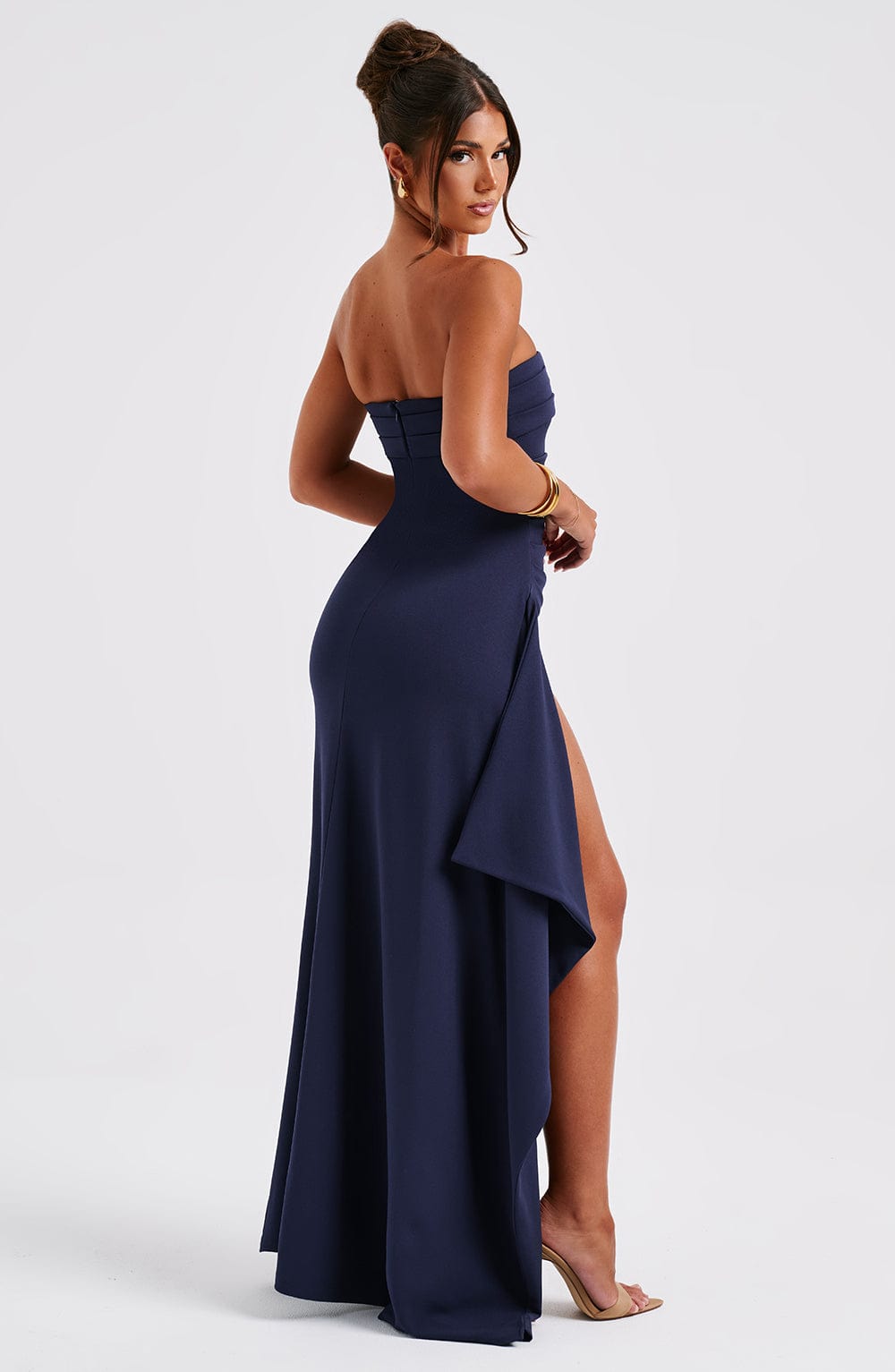 Side profile of the navy blue strapless maxi dress, emphasizing the form-fitting silhouette and dramatic high slit with draped fabric.