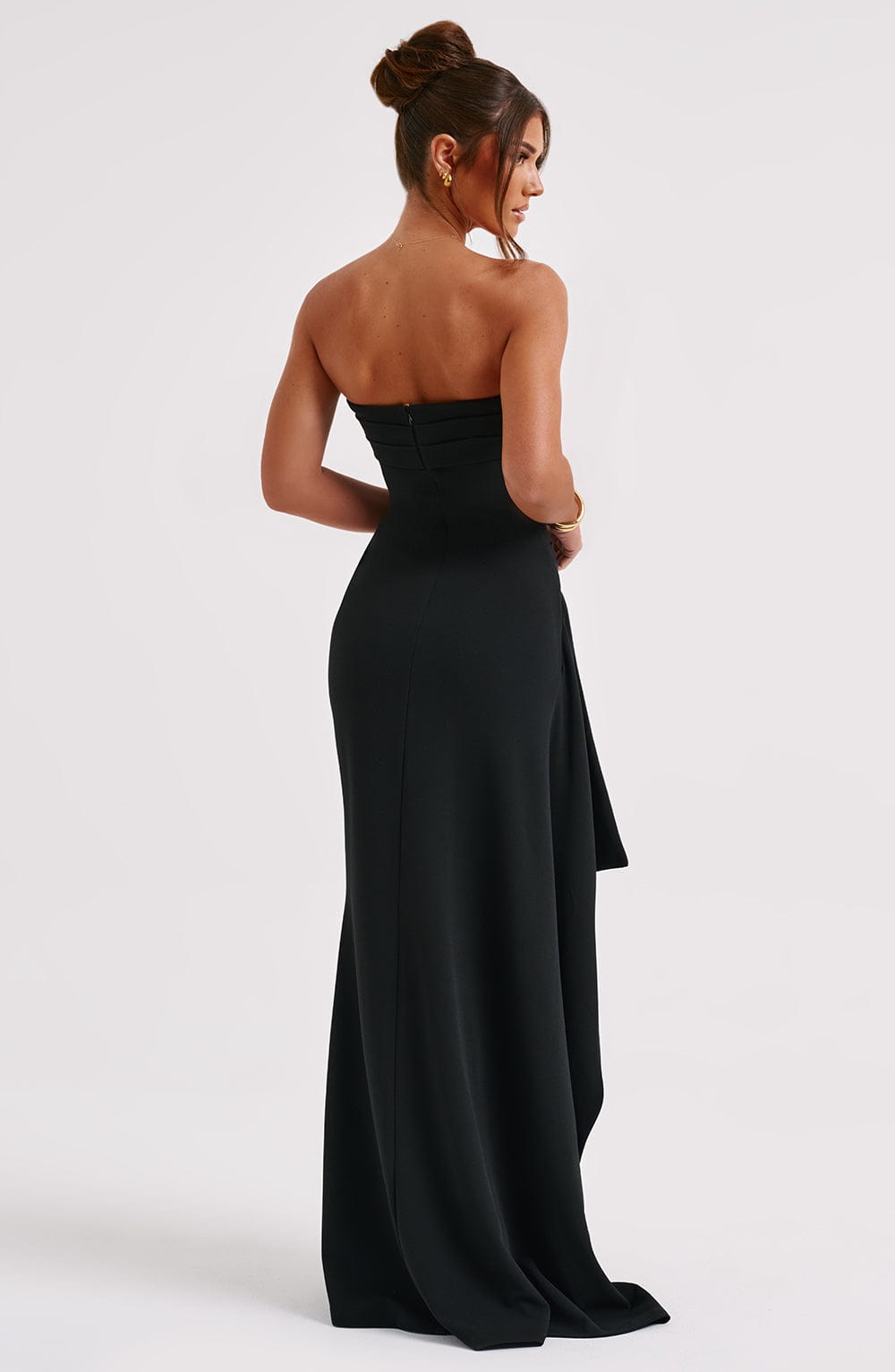 Back view of the black strapless maxi dress, showcasing the form-fitting design and the flowing draped fabric from the slit.