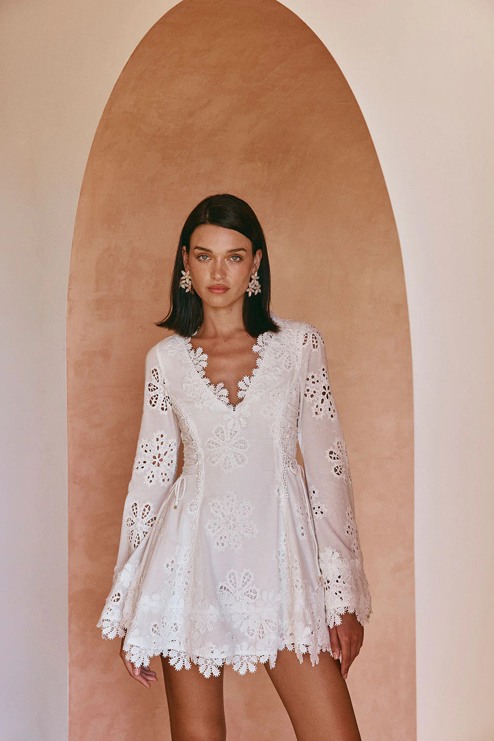 Close-up of the white lace scalloped mini dress, highlighting the V-neckline and detailed floral cutouts on the sleeves and bodice.
