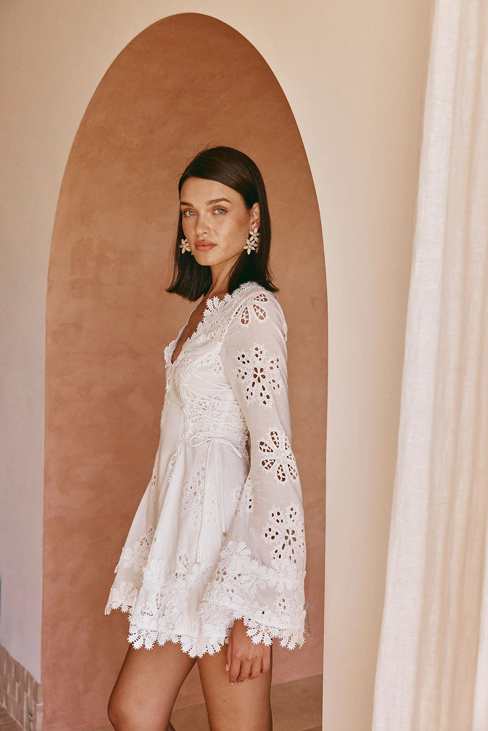 Side profile of the white lace scalloped mini dress, showcasing the flared long sleeves with cutouts and the scalloped hemline.