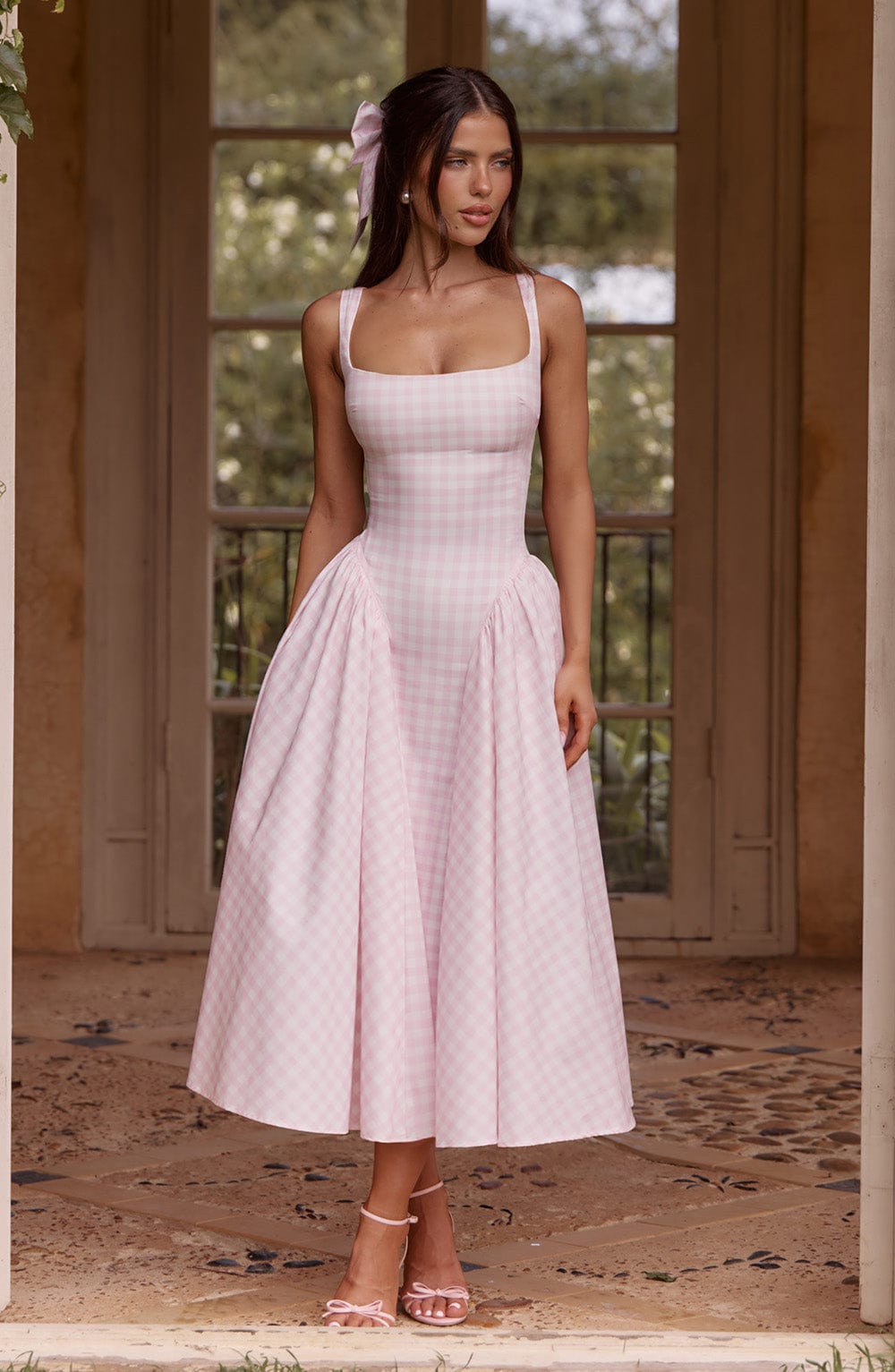 Full body view of a woman wearing a pink gingham Lana Midi Dress with a square neckline and voluminous skirt.