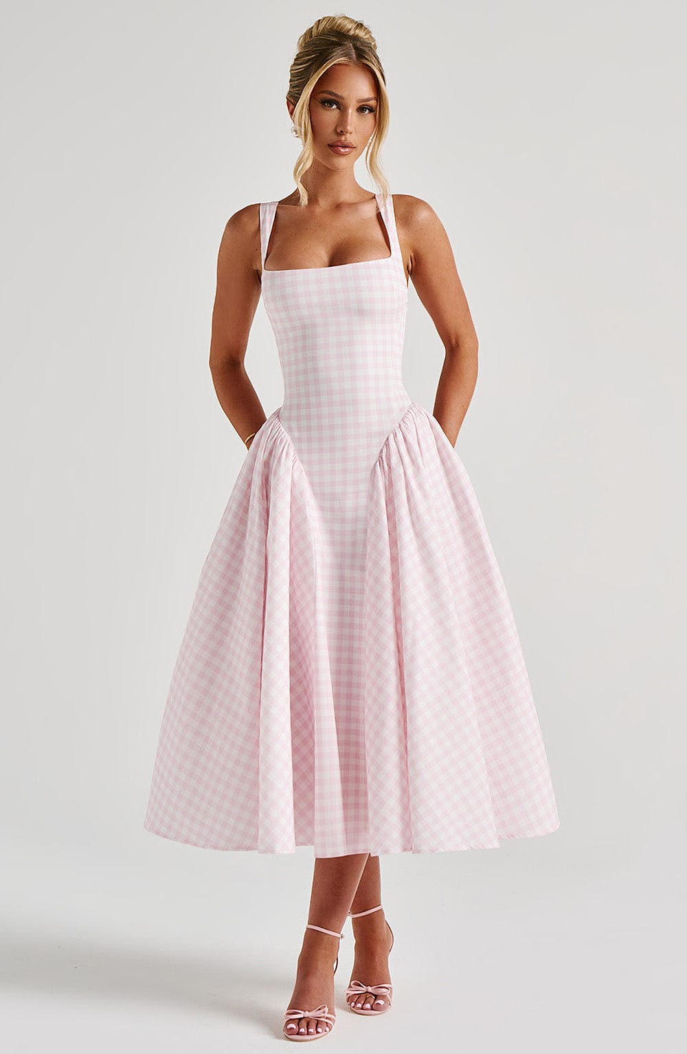 Front view of a woman posing in a pink gingham Lana Midi Dress, featuring a cinched waist and wide straps.
