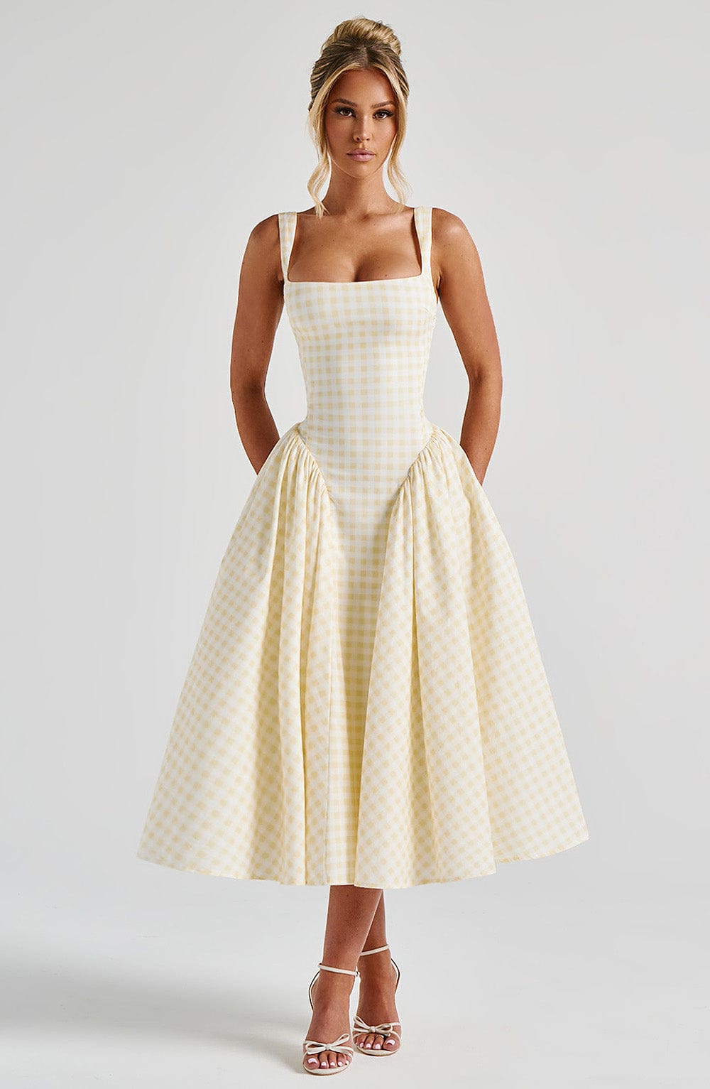 Woman in a light yellow gingham Lana Midi Dress, featuring a square neckline, fitted bodice, and pleated skirt.