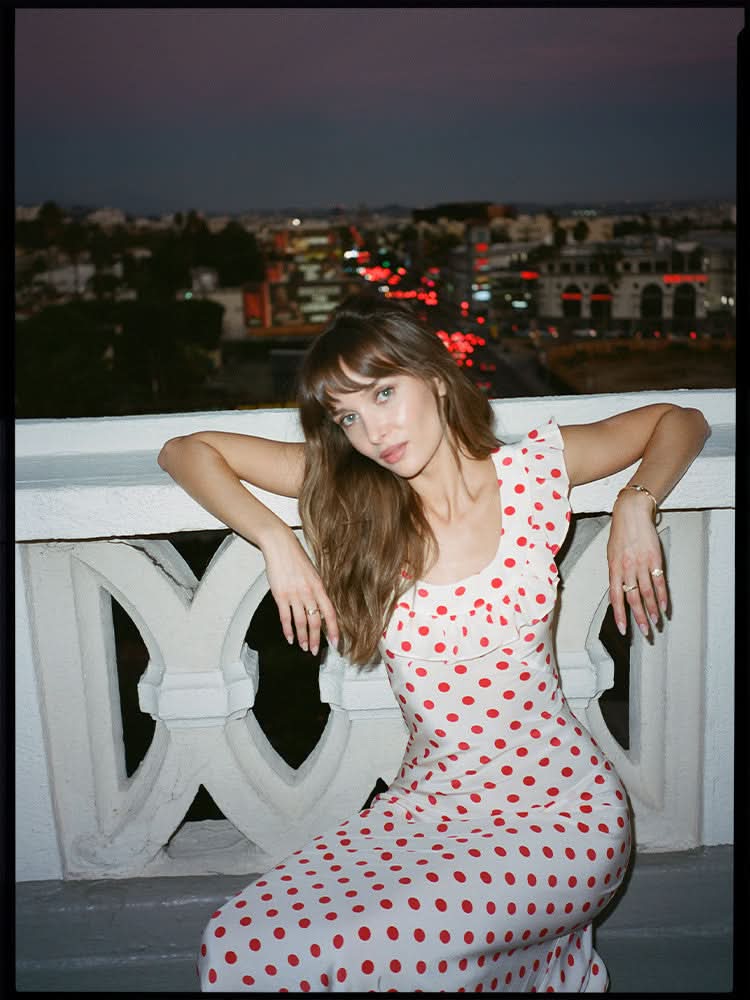 Elegant white polka dot maxi dress with ruffled cap sleeves for women, seated pose