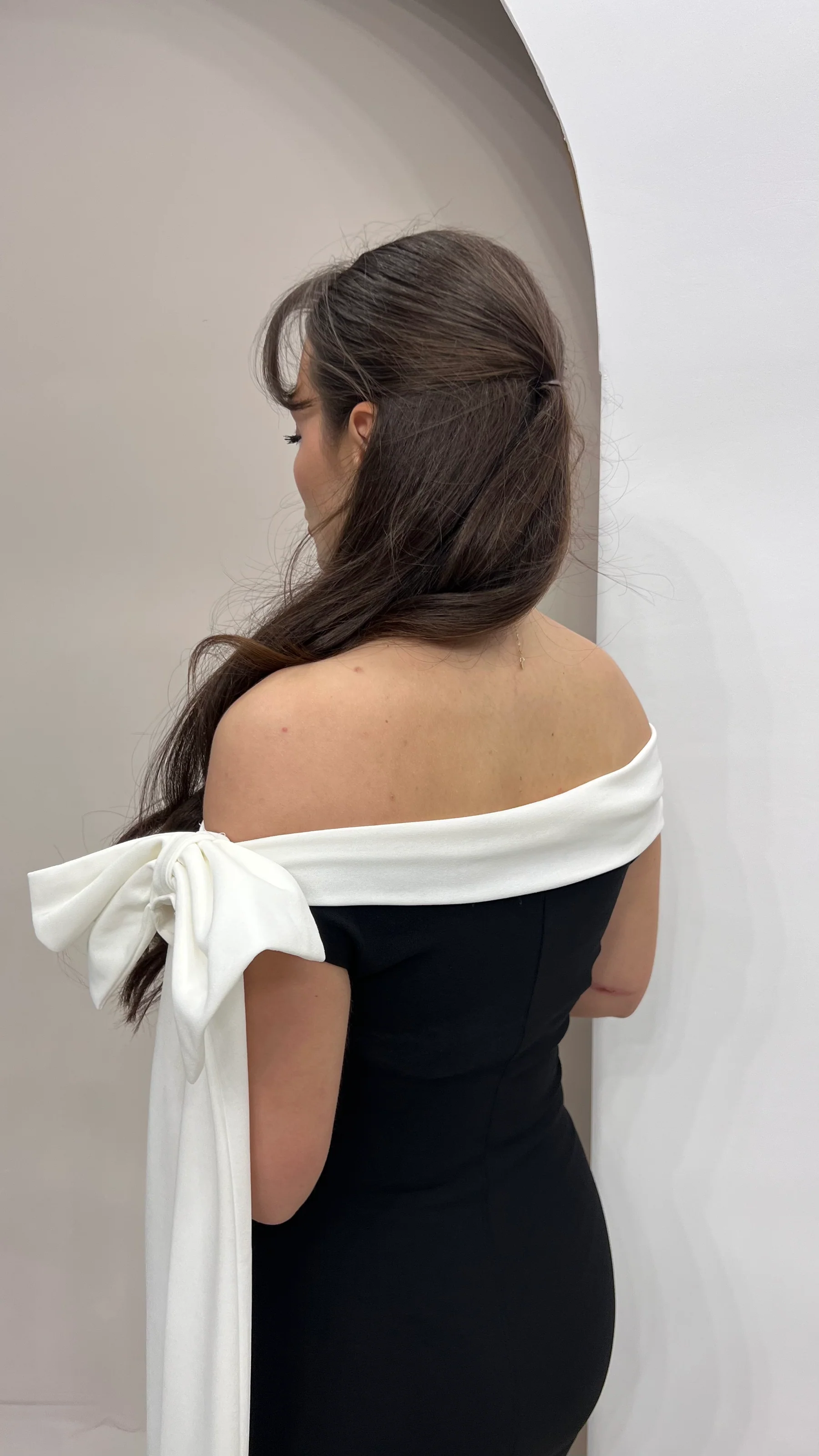 Back view of a black off-shoulder maxi dress with white trim and bow detail for women