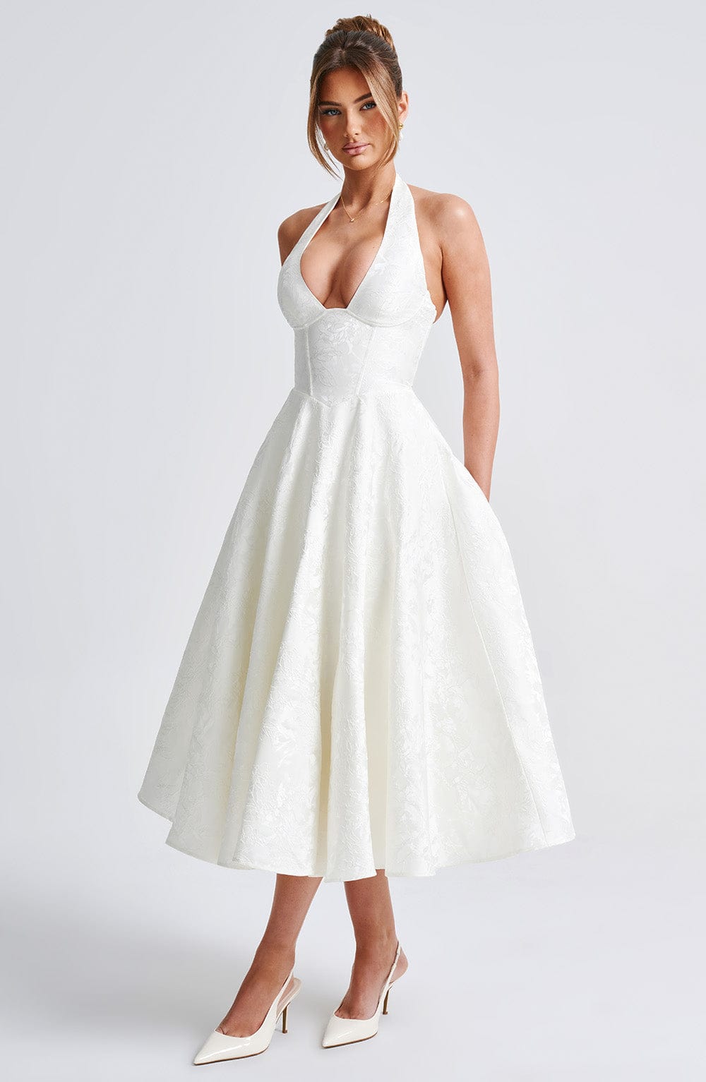 Front view of a white Leilani Halter Midi Dress with a deep V-neck and textured fabric, worn with white heels.