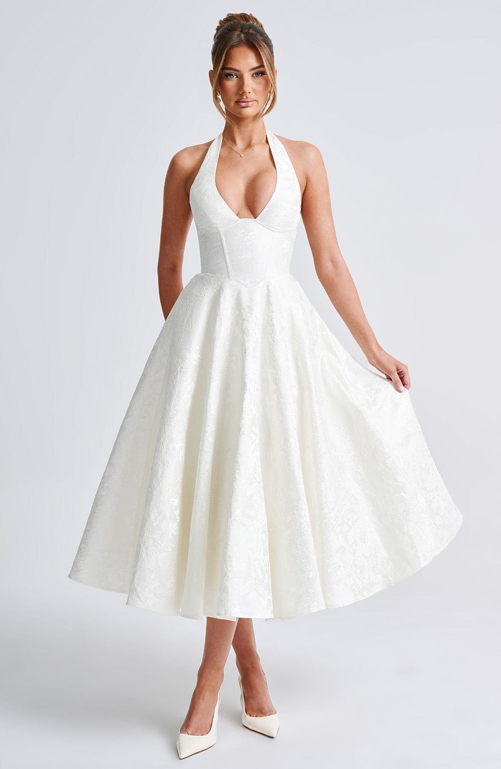 White Leilani Halter Midi Dress with a full skirt and textured floral pattern, shown with a model lifting the hem.