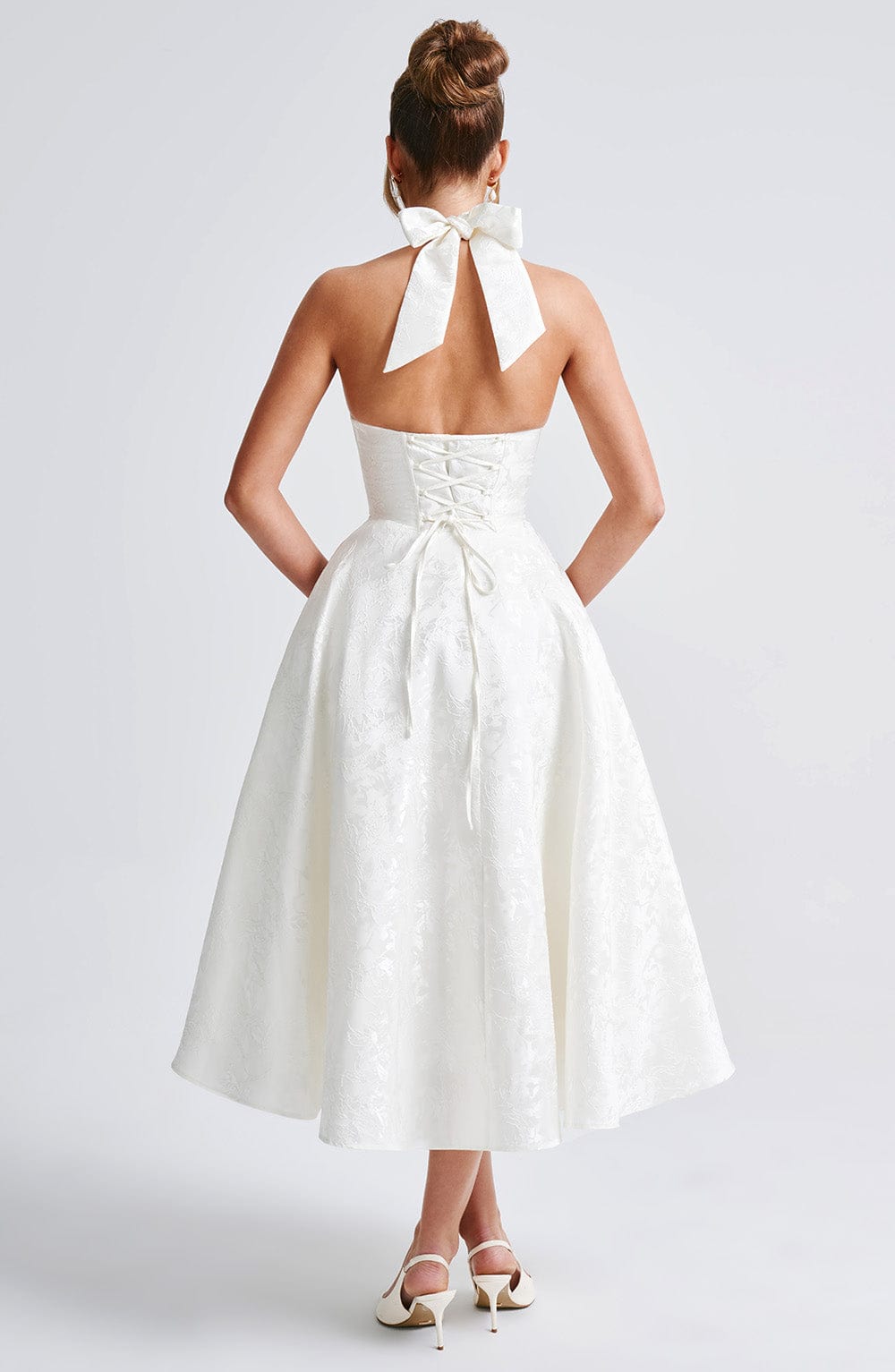 Back view of the white Leilani Halter Midi Dress featuring a large bow closure and corset-style lacing on the bodice.