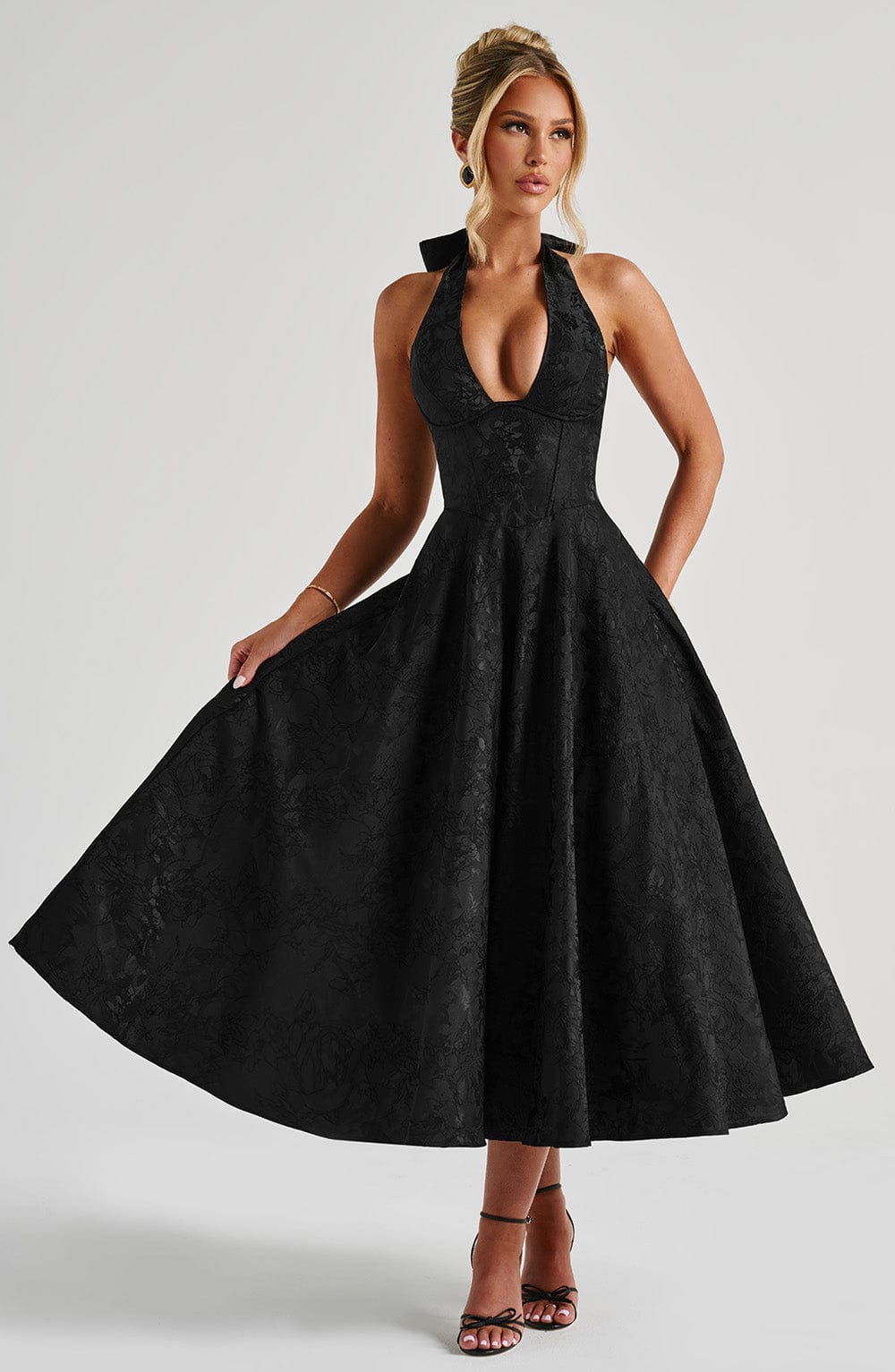 Front view of a black Leilani Halter Midi Dress with a deep plunging neckline and textured fabric, worn with black heels.