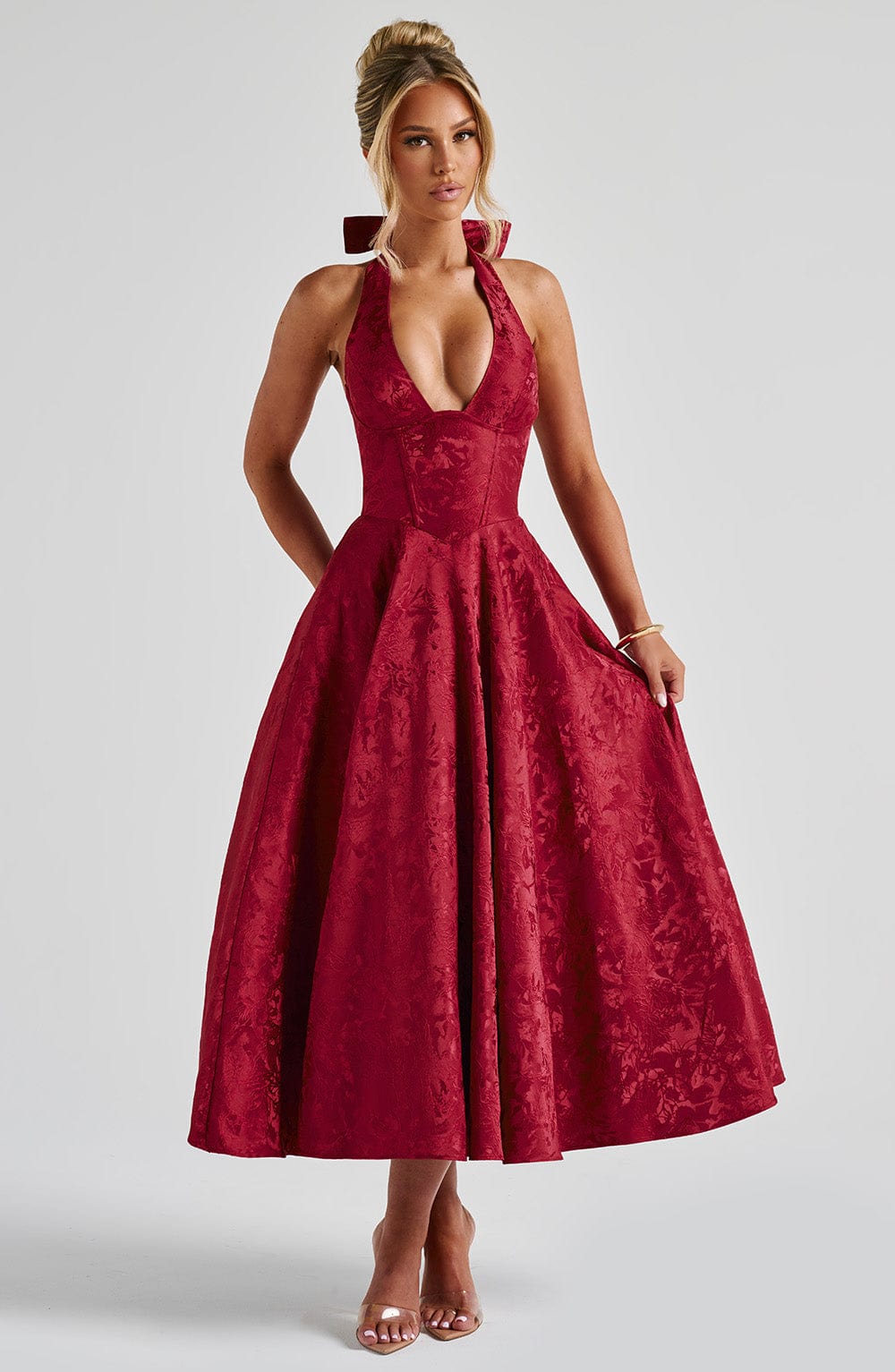Front view of a red Leilani Halter Midi Dress with a deep V-neck, textured fabric, and full skirt, worn with nude heels.