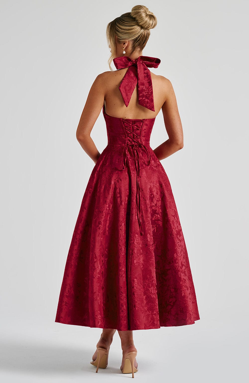 Back view of the red Leilani Halter Midi Dress, highlighting the large bow tie and corset lacing on the bodice.