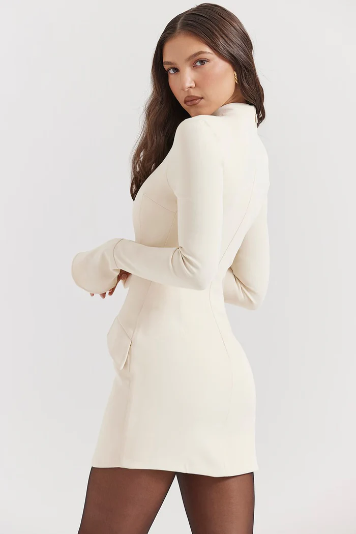 Side profile of a cream structured mini dress with long sleeves, mock neck, and visible hip pockets, paired with dark tights.