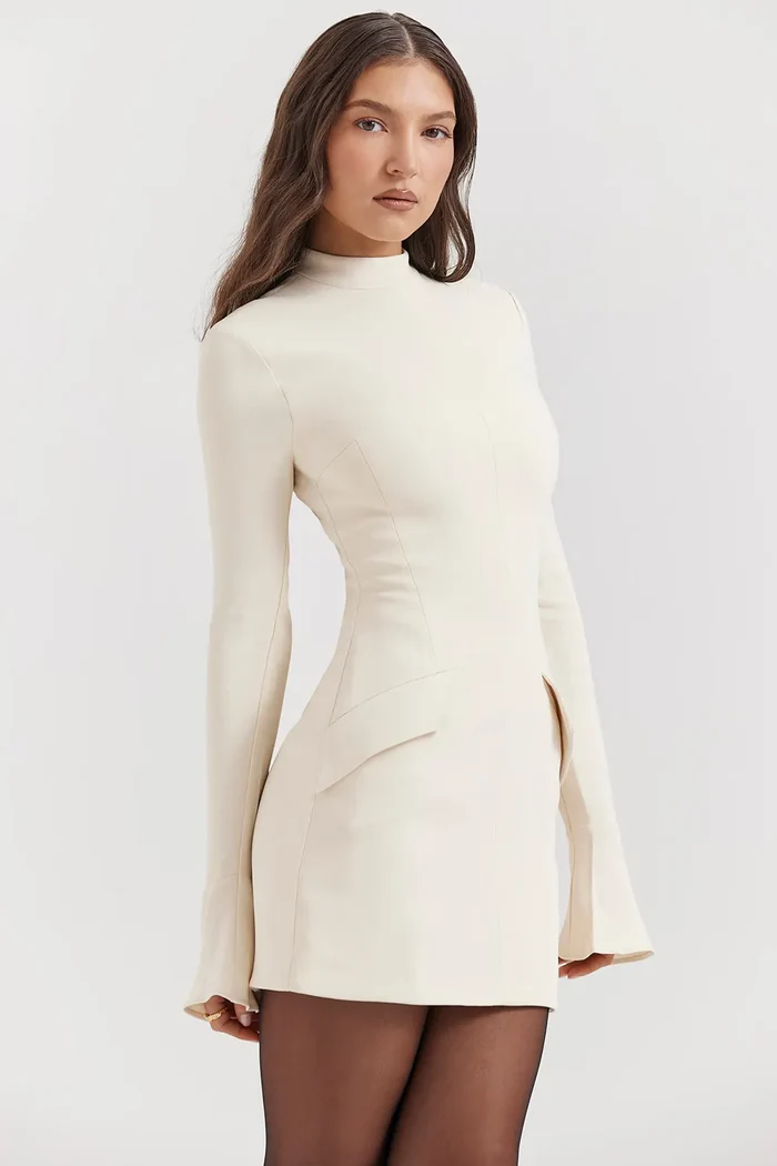 Angled front view of a cream structured mini dress, displaying the mock neck, long sleeves, and unique hip pocket flaps.