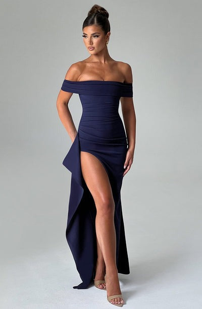 Full body view of a navy blue off-the-shoulder maxi dress with a thigh-high slit and cascading ruffle detail.