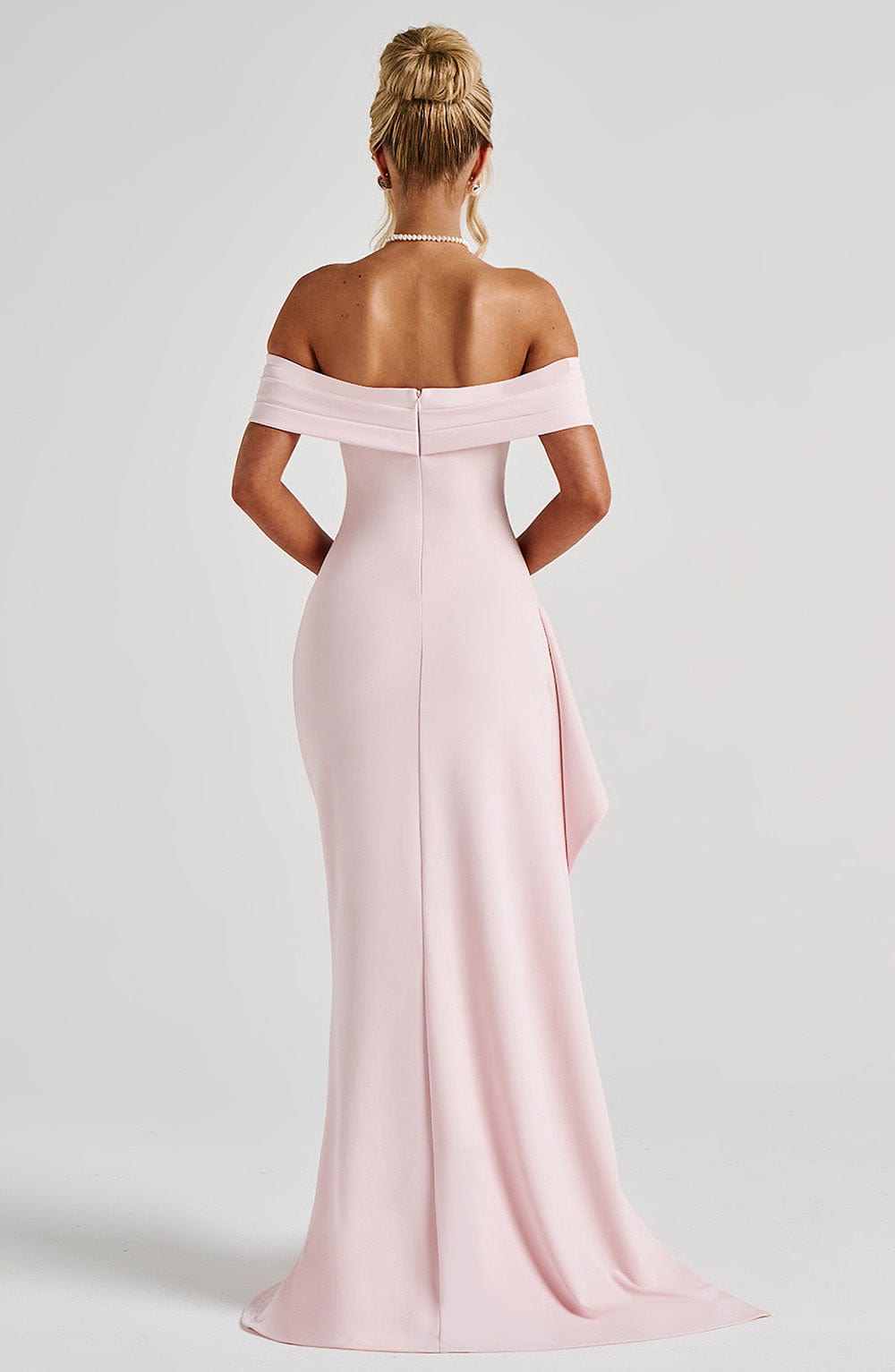 Back view of a light pink off-the-shoulder maxi dress, showing the fitted silhouette and subtle train.