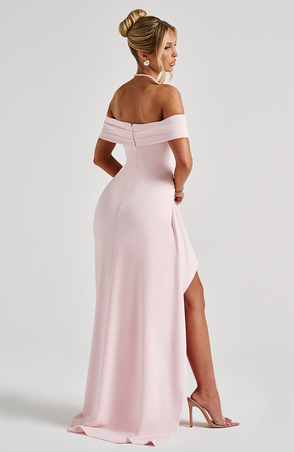 Rear side view of a light pink off-the-shoulder maxi dress with a high slit and a slight train