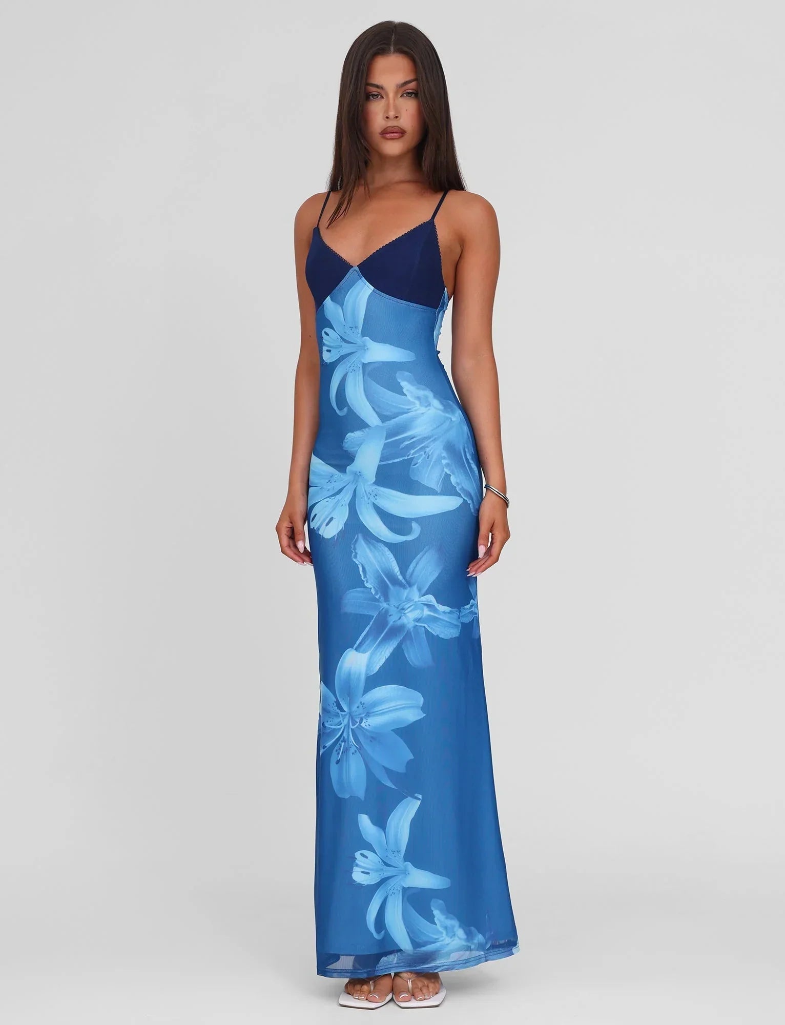 Front view of a woman in a blue floral maxi dress with spaghetti straps on a white background.