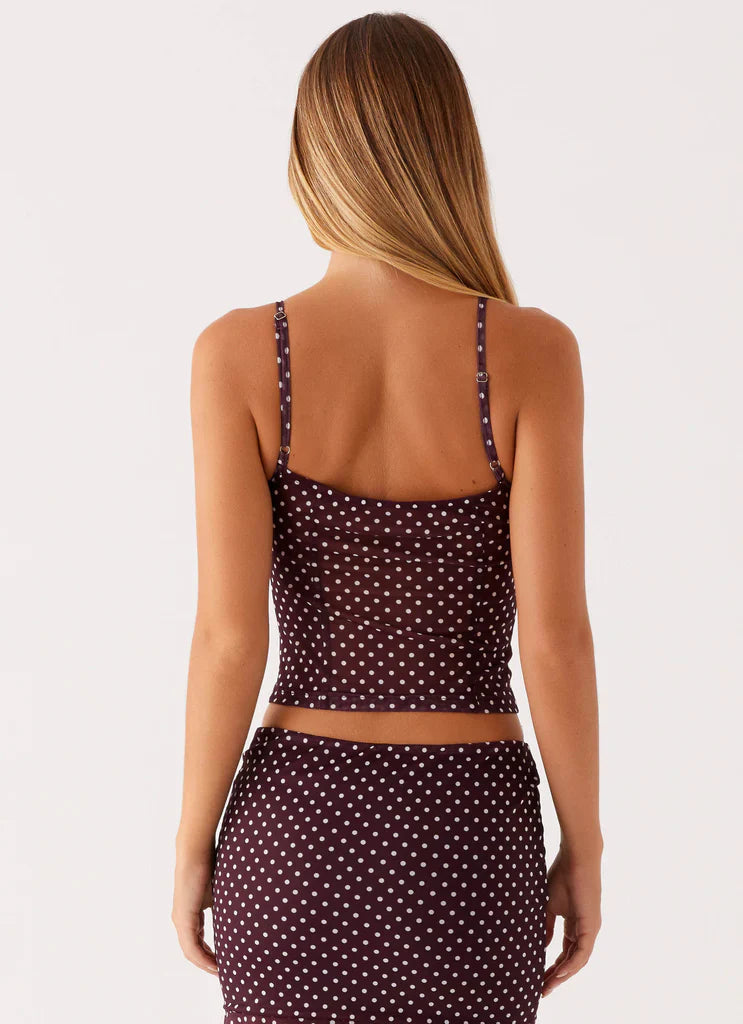 Back view of woman in burgundy polka dot midi set featuring spaghetti strap top and skirt