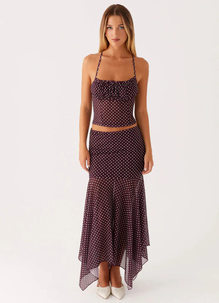 Woman in full shot wearing a dark purple polka dot ruched crop top and asymmetrical midi skirt for women