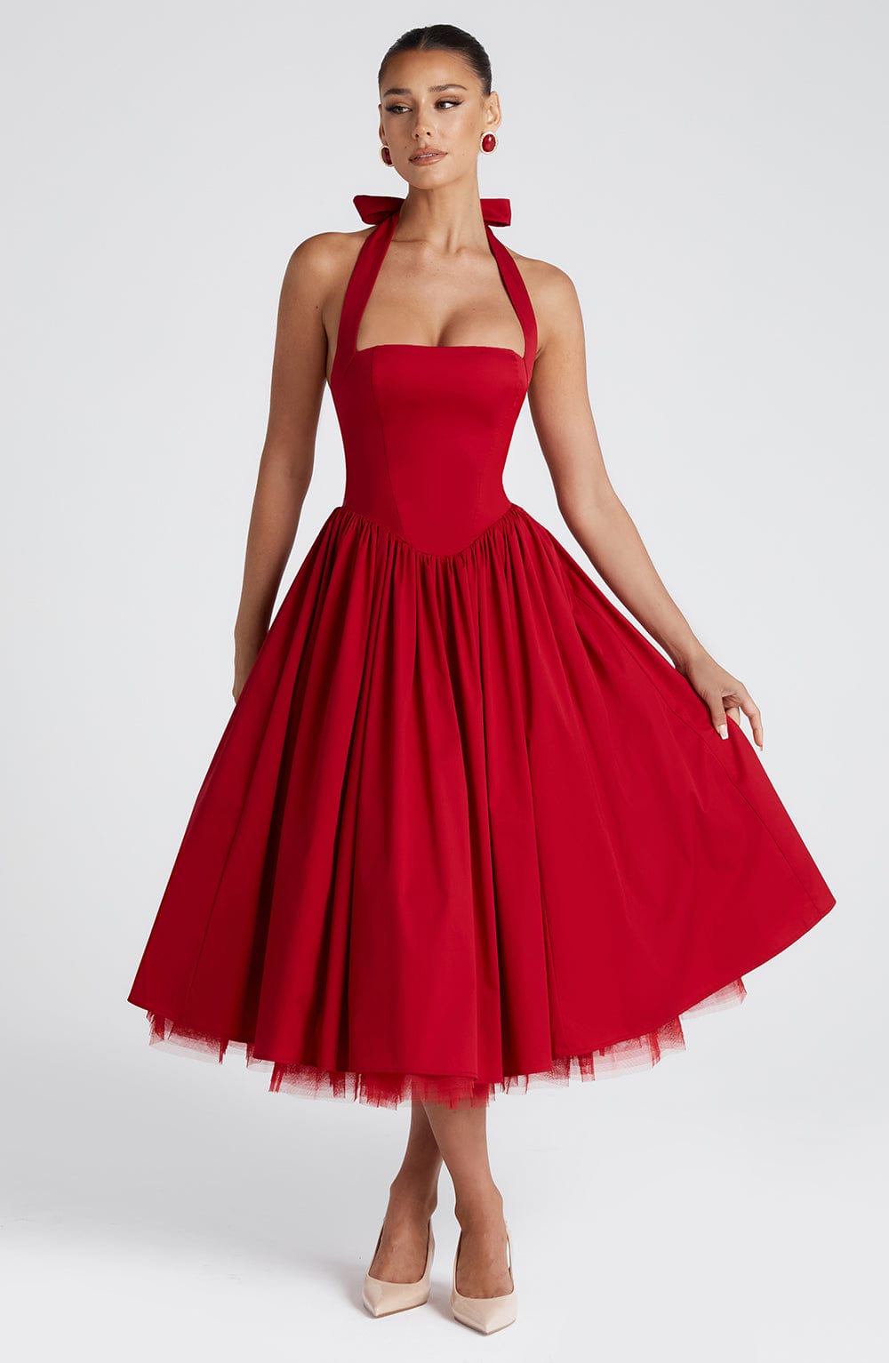 Red halter midi dress with a full pleated skirt, showing a hand gently touching the fabric, highlighting the flow of the dress.