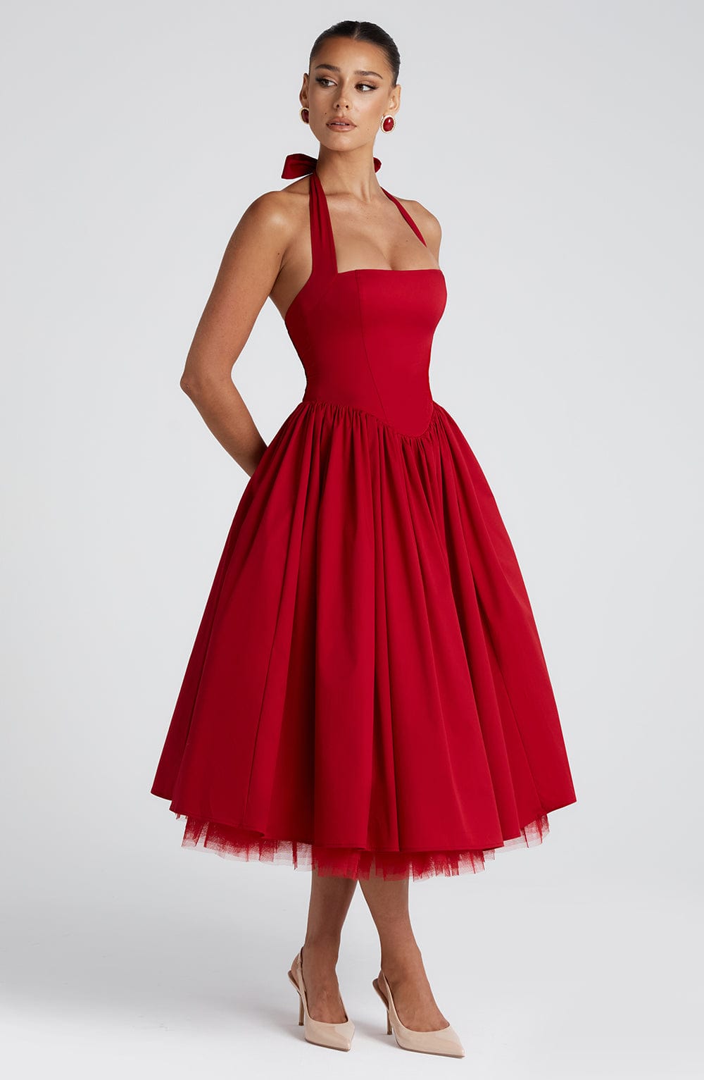 Side view of a red halter midi dress, showcasing the structured bodice and voluminous pleated skirt with a visible tulle lining.