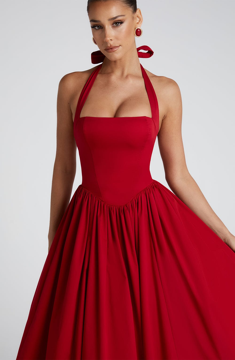 Close-up of the bodice and upper skirt of a red halter midi dress, featuring a square neckline and gathered waist detail.