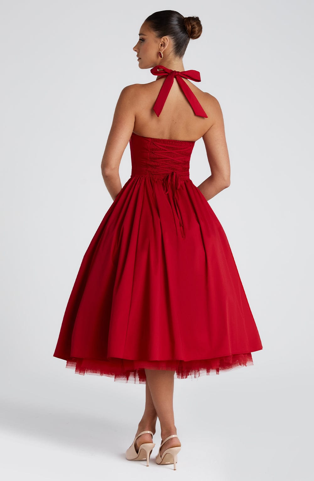 Back view of a red halter midi dress, showcasing the tied neck bow, smocked back, and full pleated skirt with a visible tulle underlay.